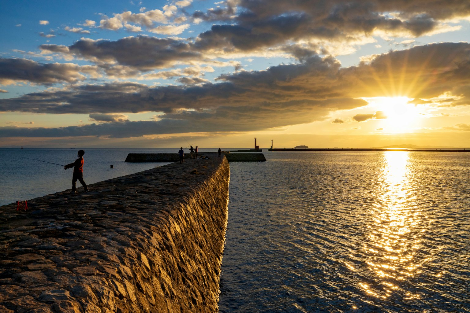 Una persona caminando sobre un muelle de piedra con una hermosa puesta de sol de fondo