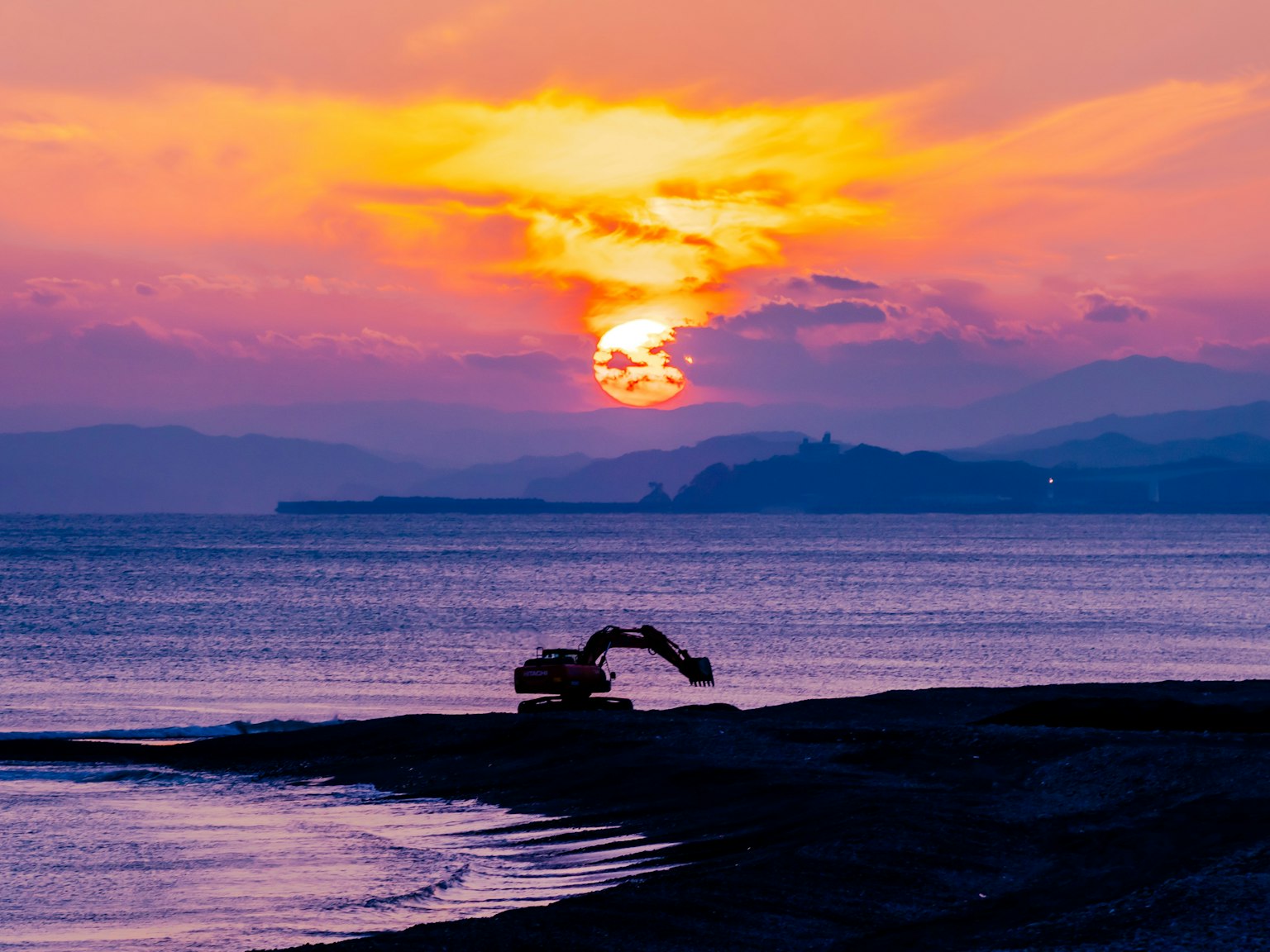 Stupendo tramonto sull'oceano con una macchina che lavora sulla spiaggia