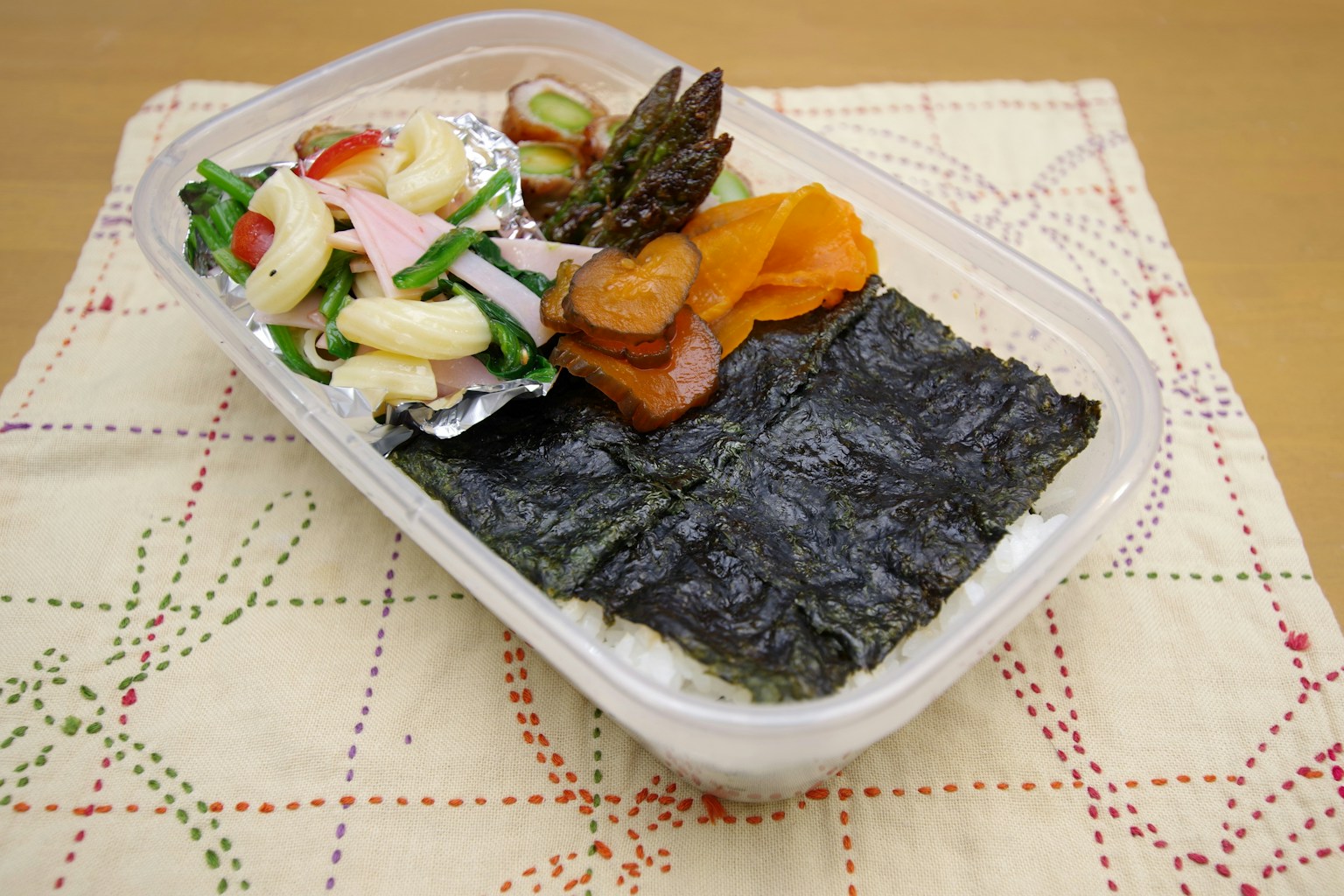お弁当箱に盛り付けられた海苔、野菜、ハム、ニンジン、果物の色とりどりの料理