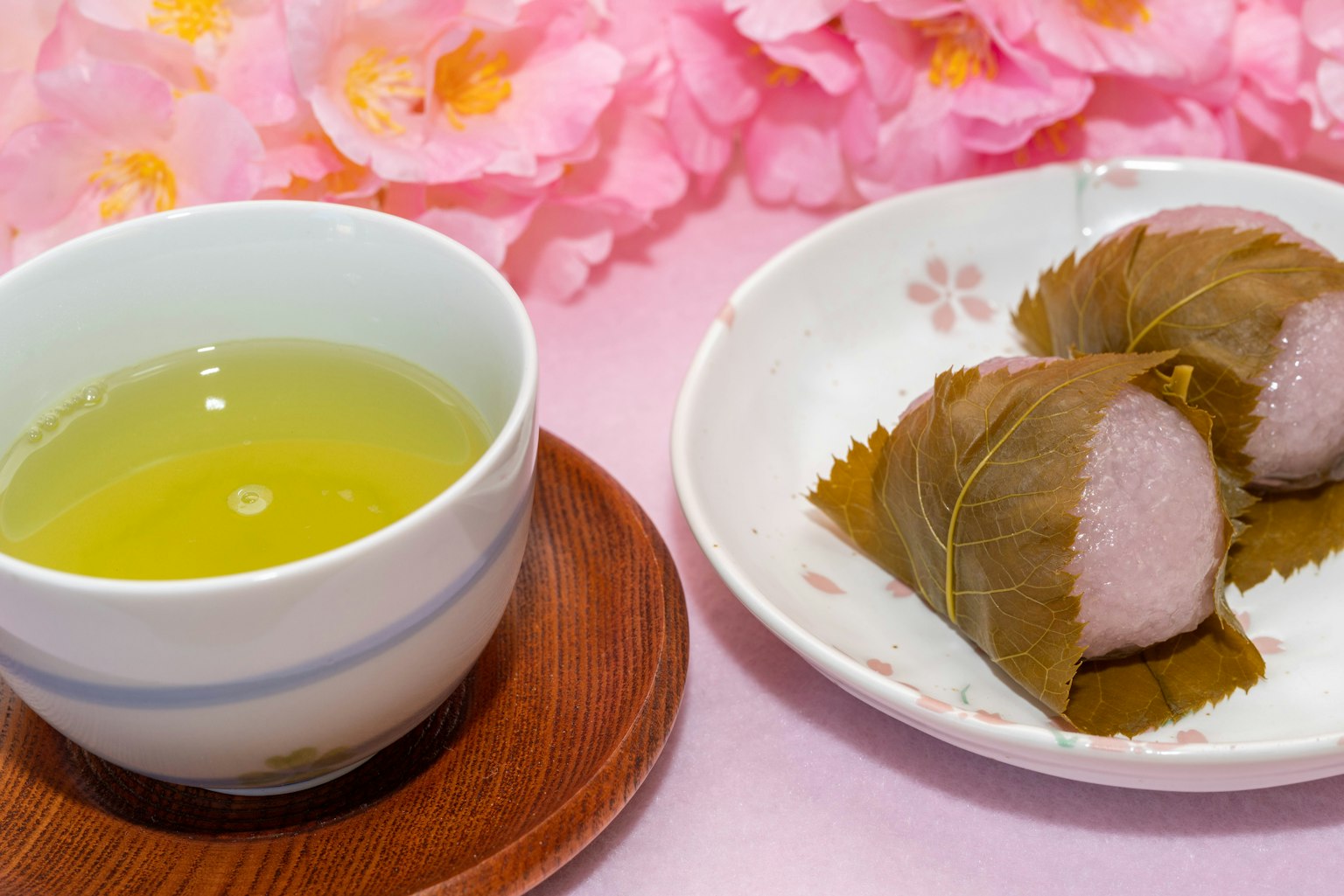 绿茶和樱花麻糬的美丽摆盘，背景为粉色花卉