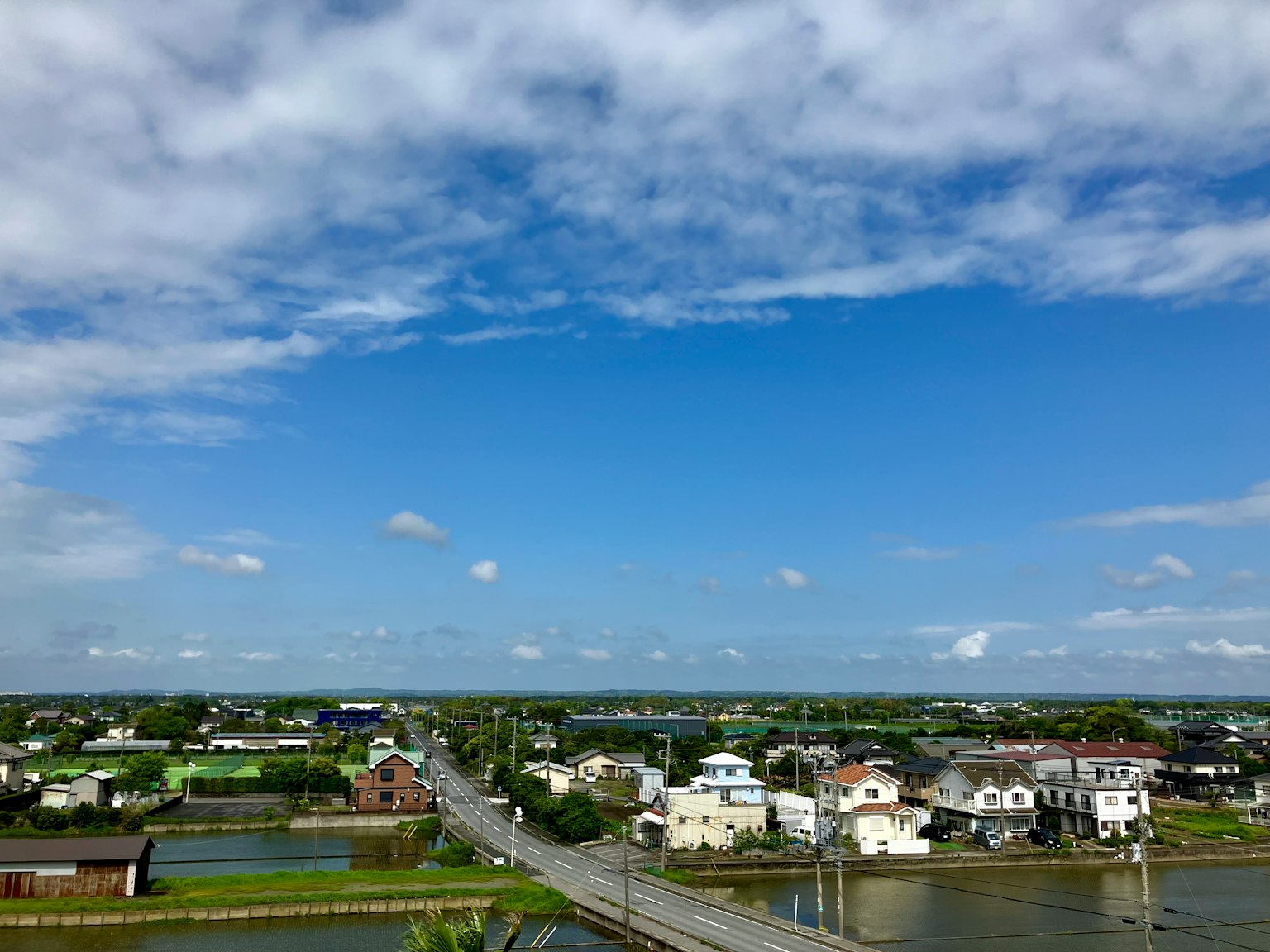 Cảnh quan với bầu trời xanh và mây trắng những ngôi nhà rải rác trên cánh đồng xanh và một cây cầu