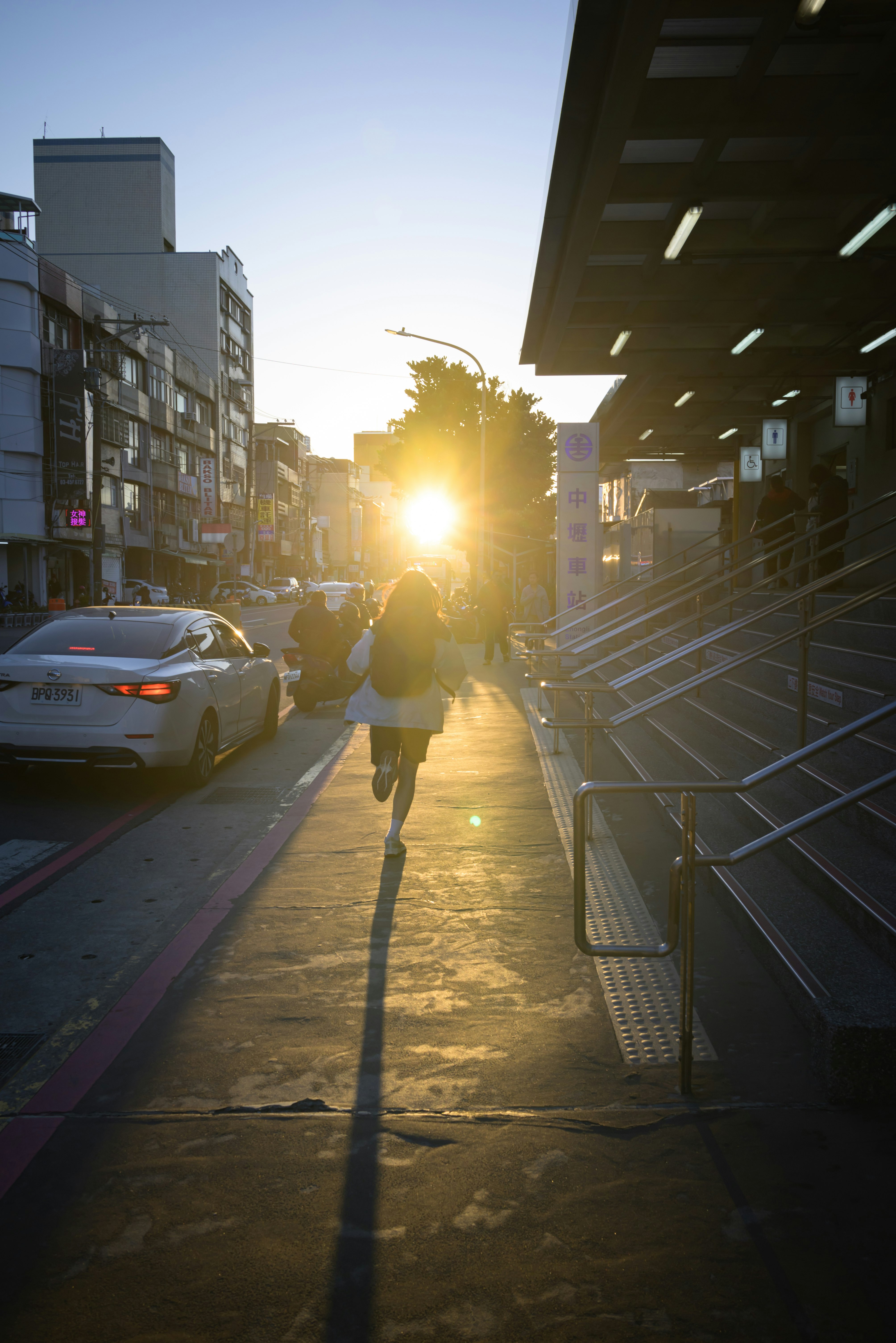 夕日に照らされた高架下の路地を歩く人々