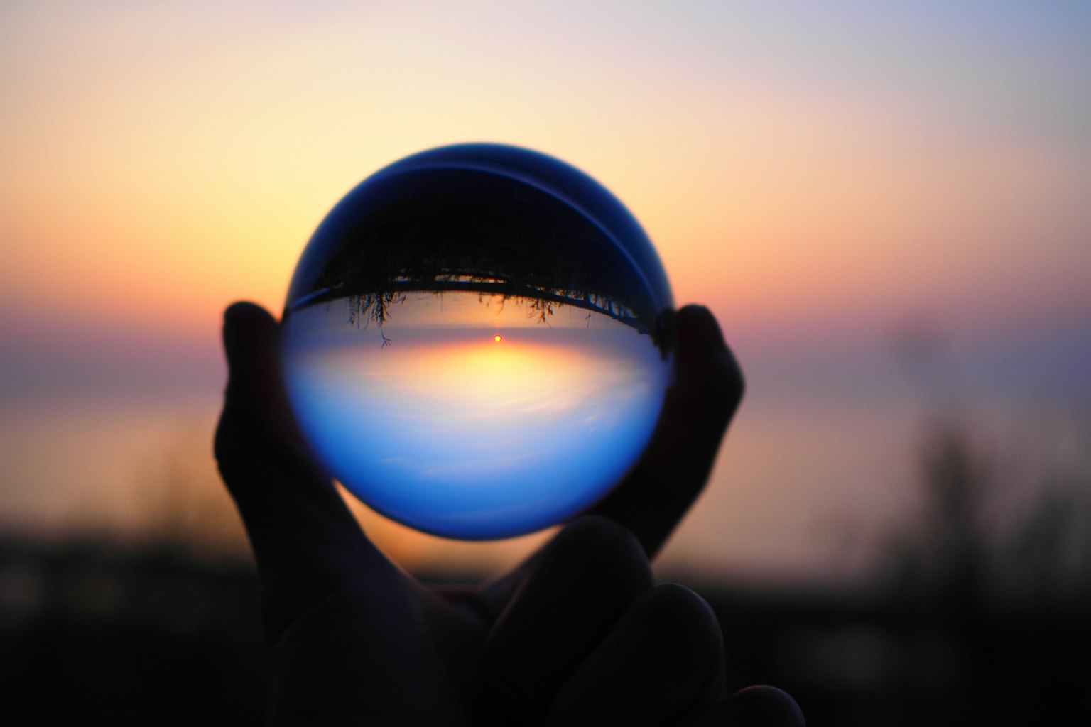 Sebuah bola kaca yang dipegang di tangan mencerminkan matahari terbenam yang indah