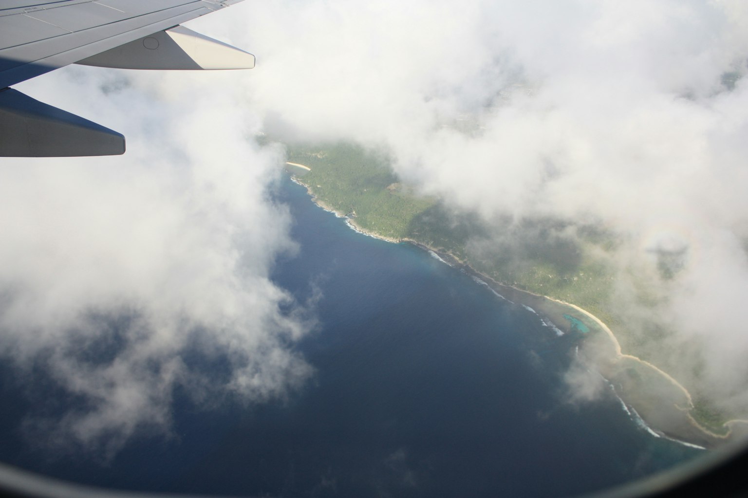 Aerial view of an island surrounded by clouds with part of an airplane wing visible
