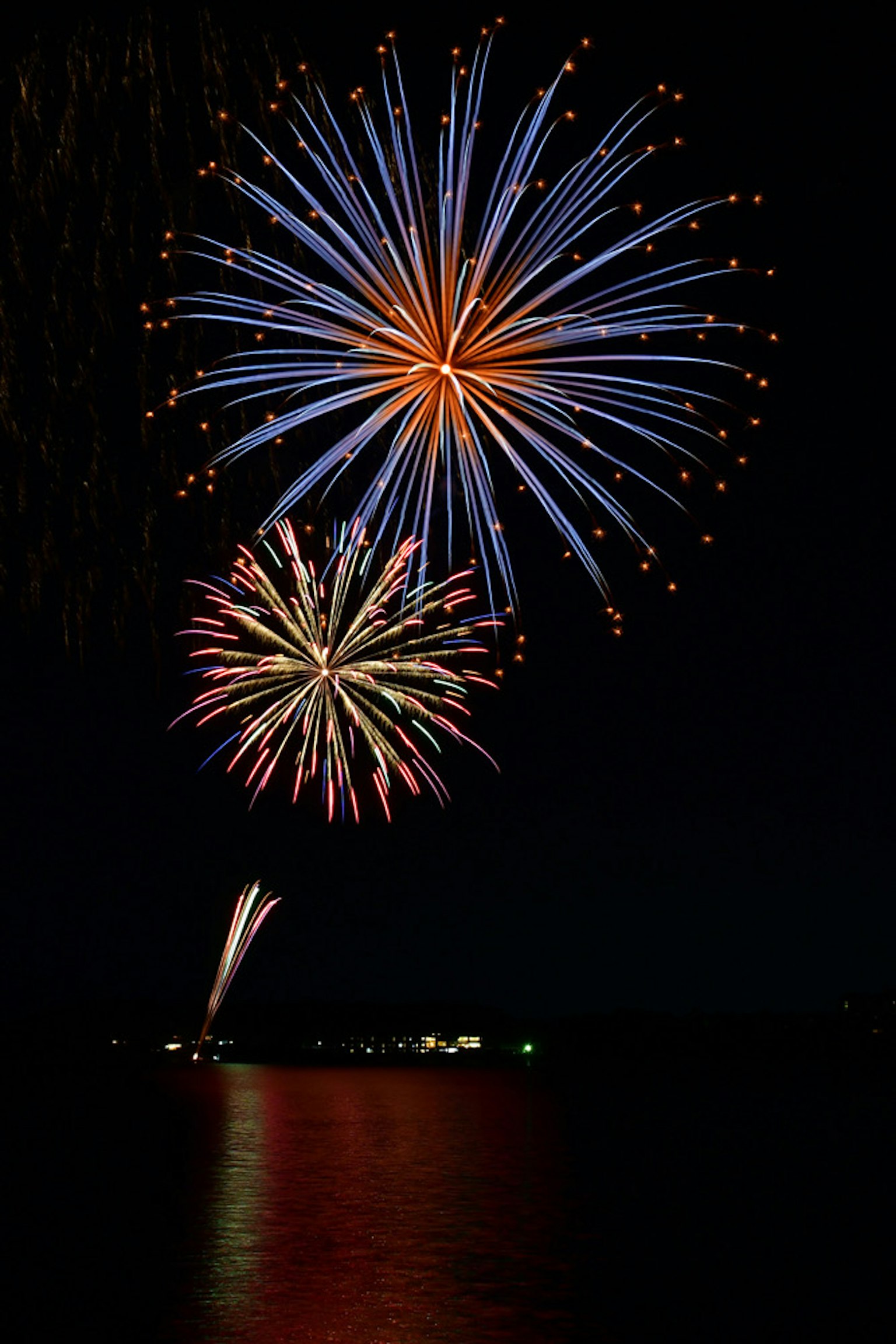 Colorful fireworks bursting in the night sky with a reflection on water