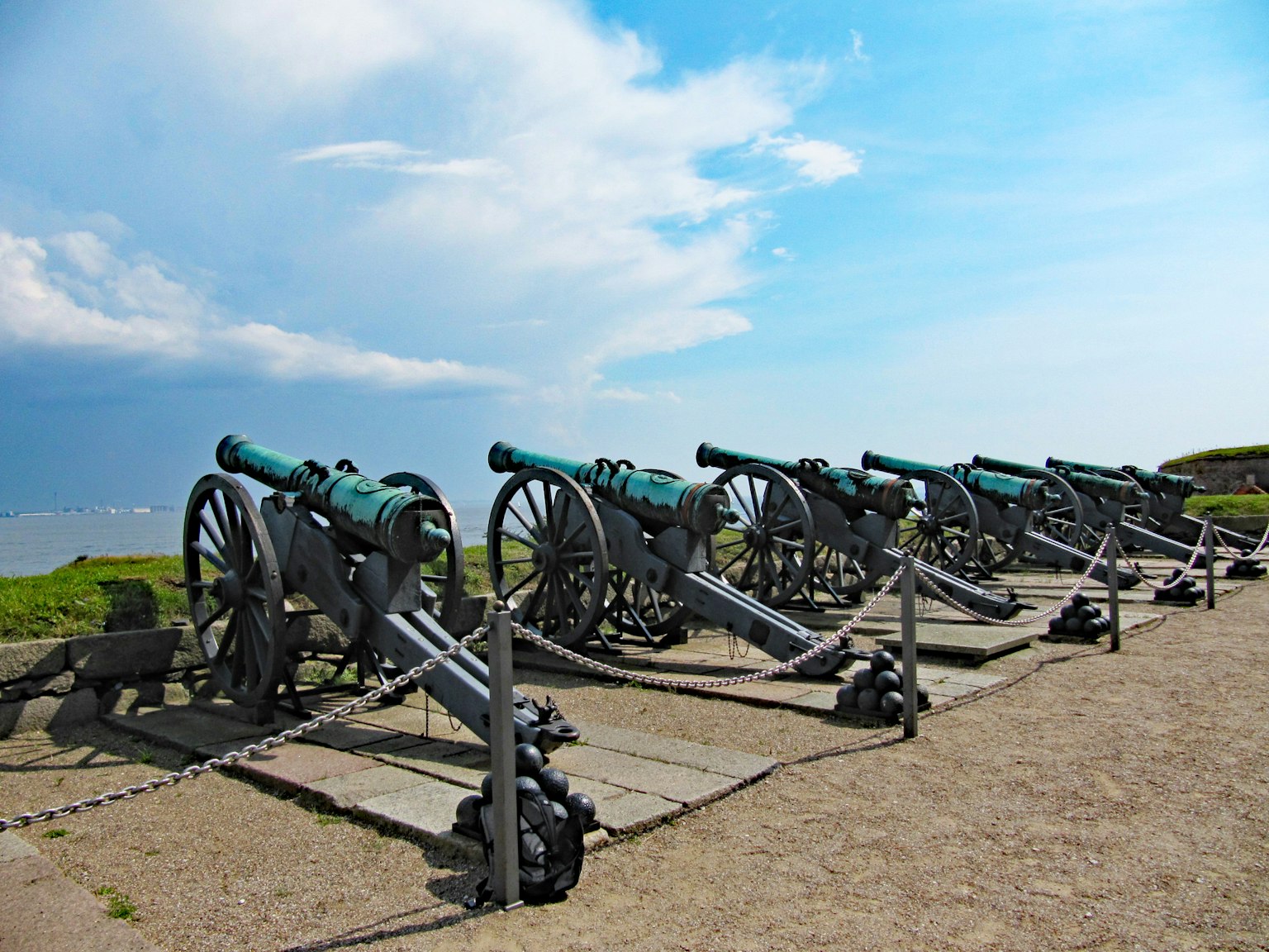Fila de cañones históricos bajo un cielo azul con hierba verde