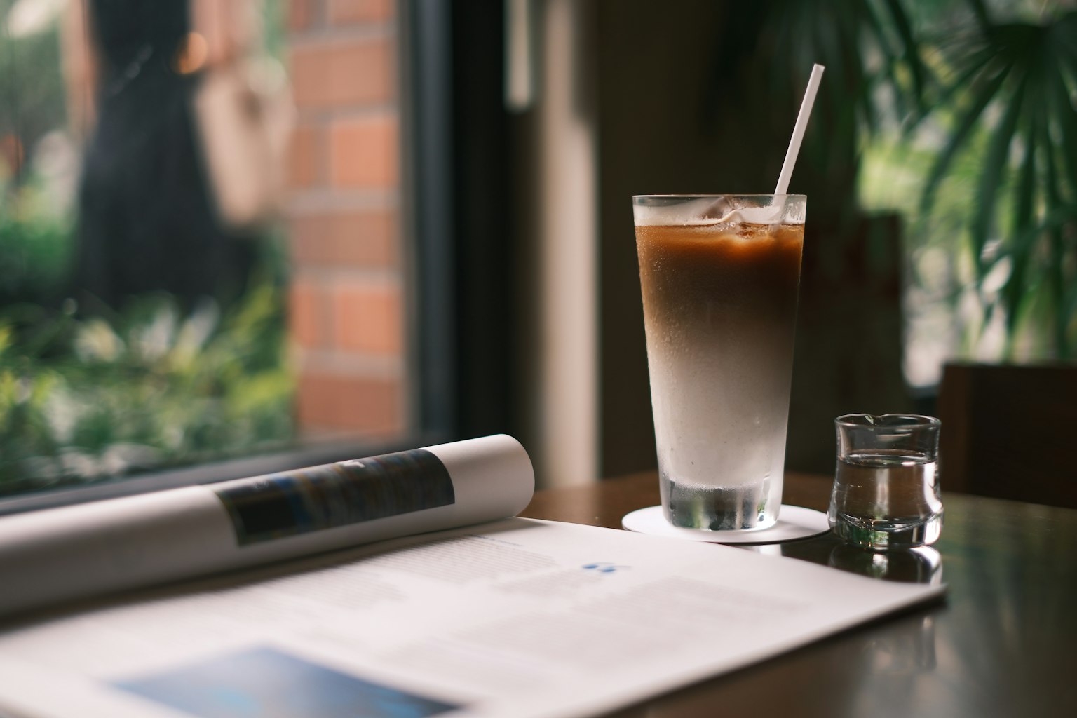 A glass of iced coffee with layered colors beside a newspaper on a cafe table