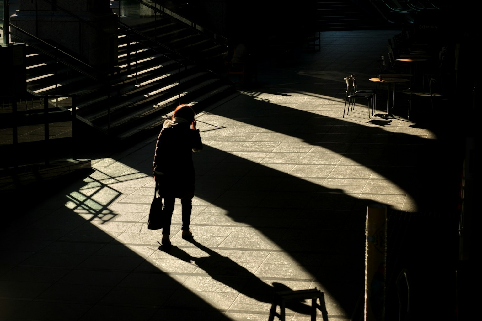 Silhouette di una persona che cammina in uno spazio tranquillo con ombre e luce che si incrociano