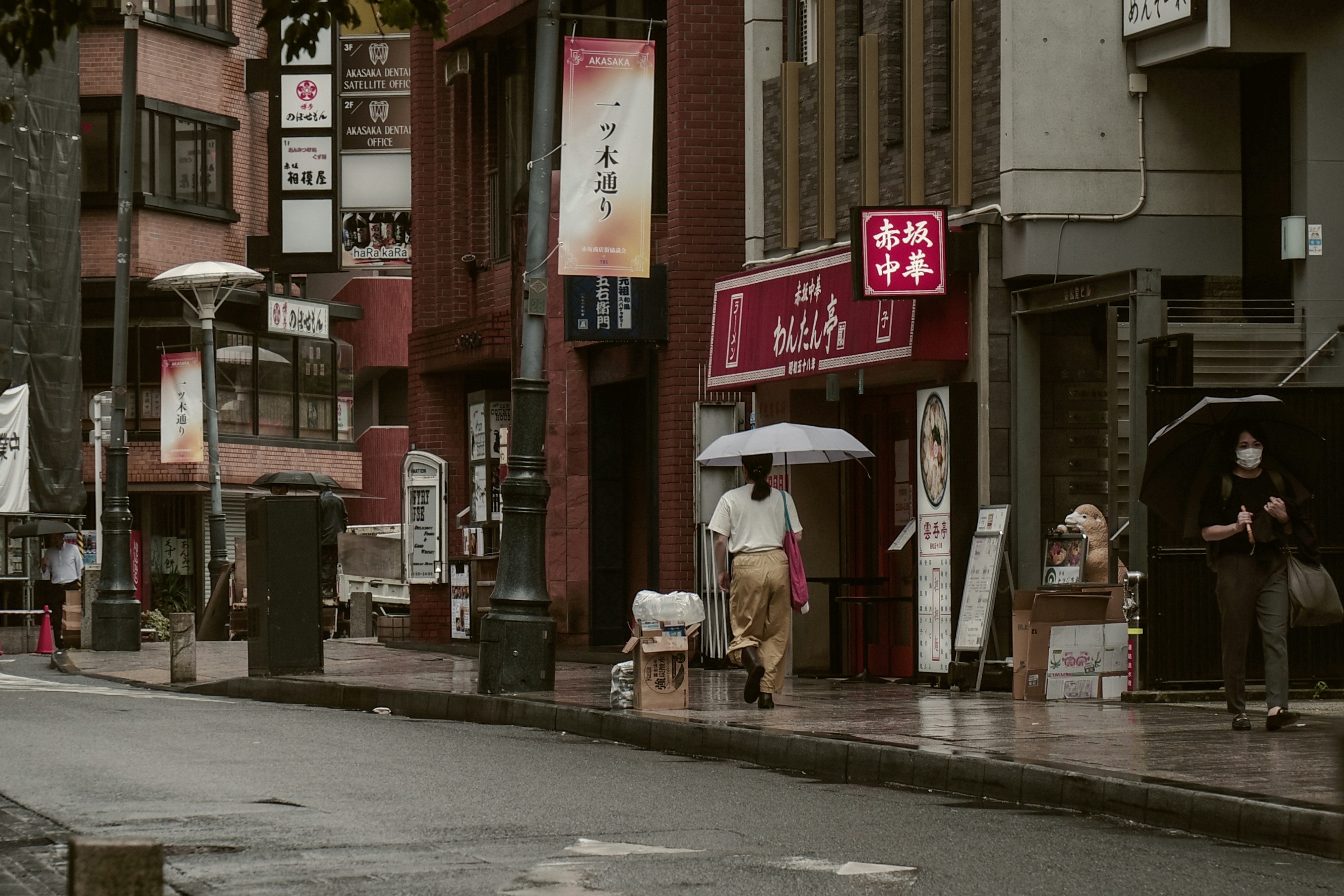 雨の赤坂の路地で傘をさす人々のある街並み