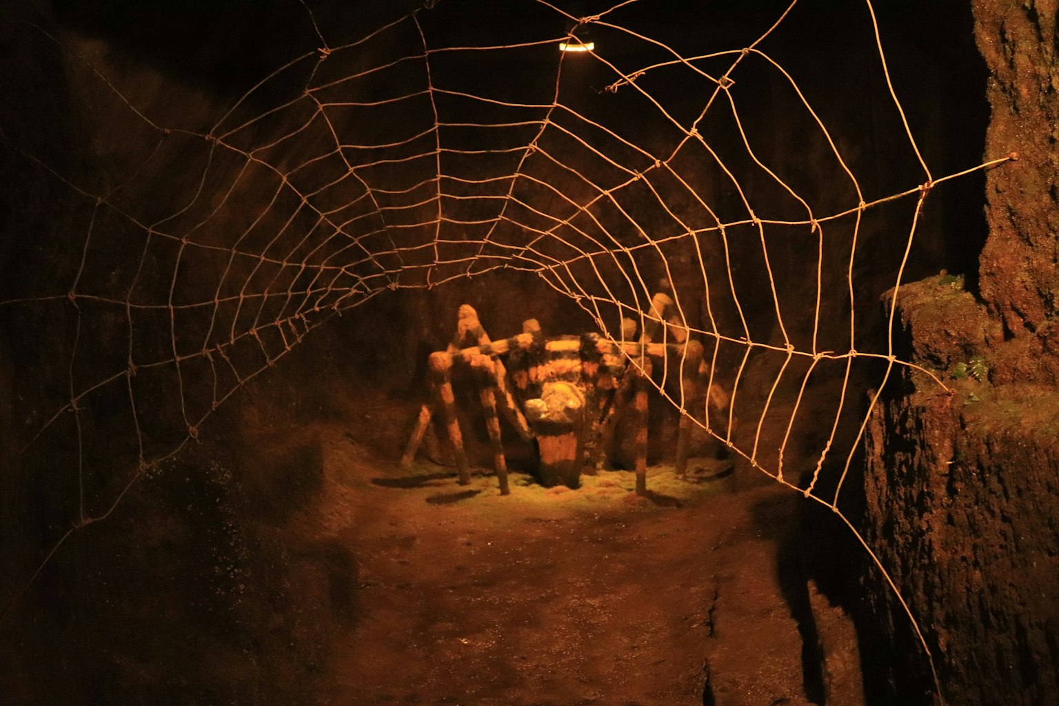 Une grande toile d'araignée dans une grotte sombre avec des silhouettes en arrière-plan