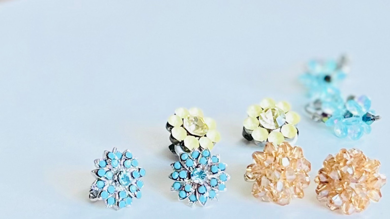 Anting berbentuk bunga berwarna biru dan emas tersusun di atas permukaan