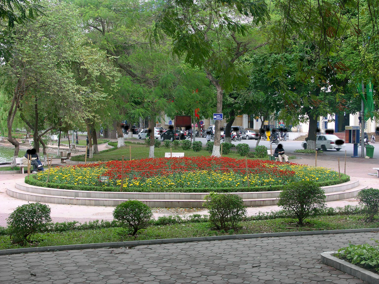 Runder Blumenbeet in einem Park mit bunten Blumen umgeben von grünen Bäumen und Bänken
