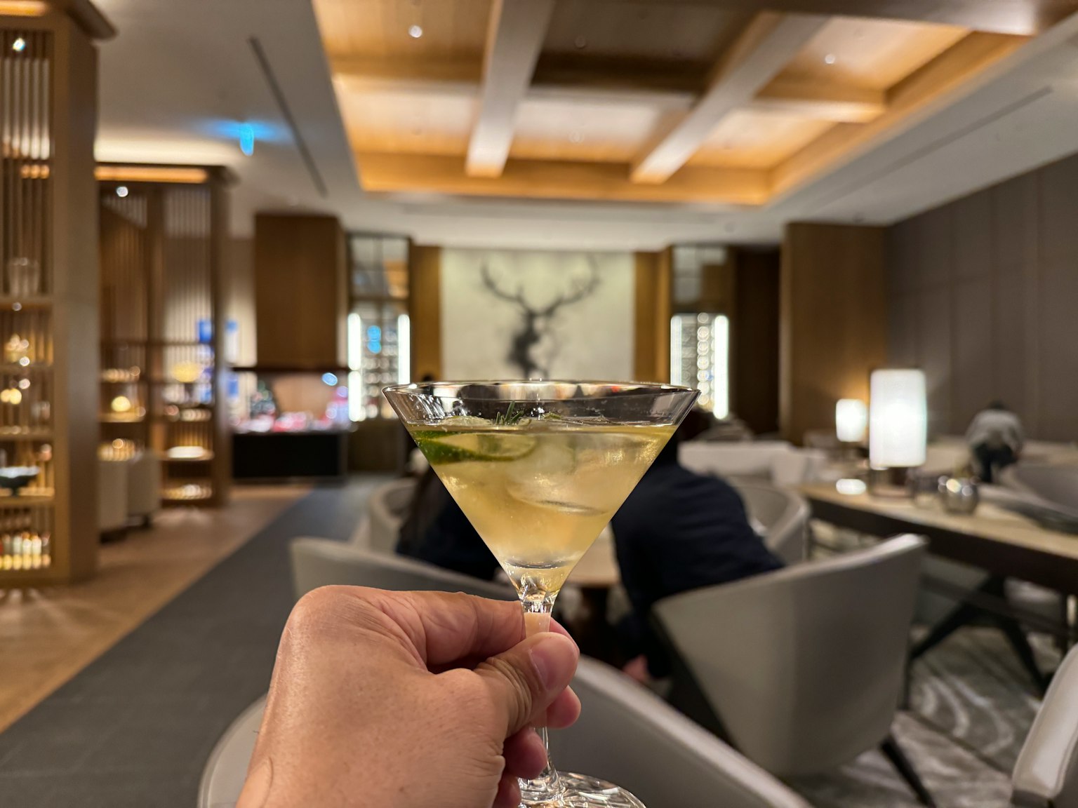 Una mano che tiene un cocktail in un lussuoso salotto con decorazioni eleganti e illuminazione soffusa
