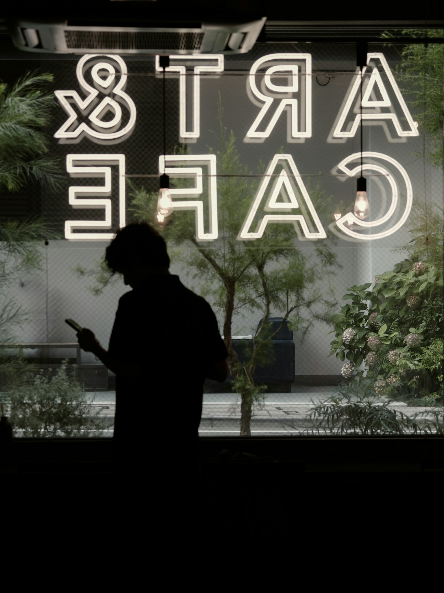 Silhouette of a person standing in front of a cafe window with neon sign reading Arts Cafe