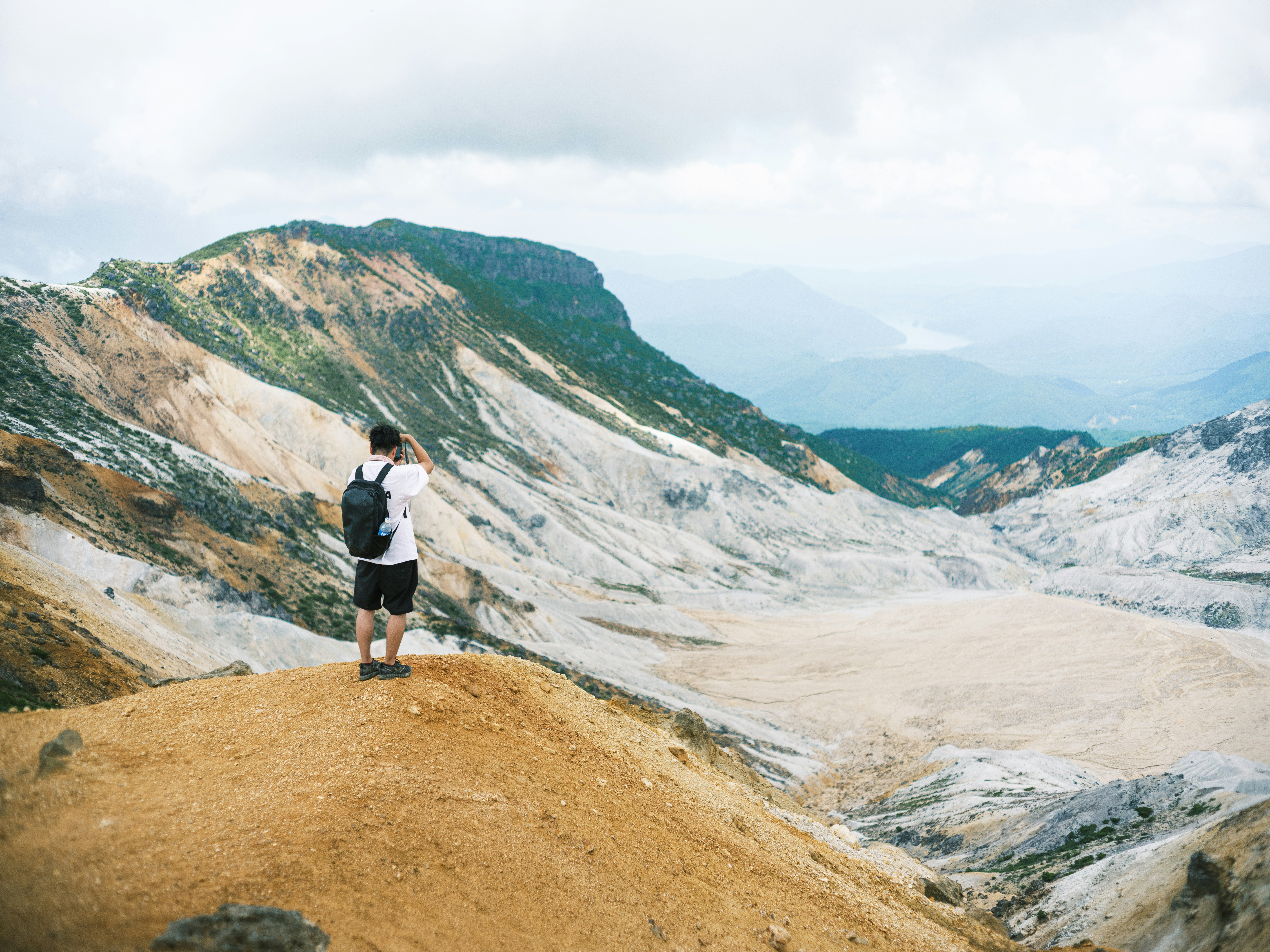 火山性の荒れ地を見下ろす登山者と広がる山岳渓谷