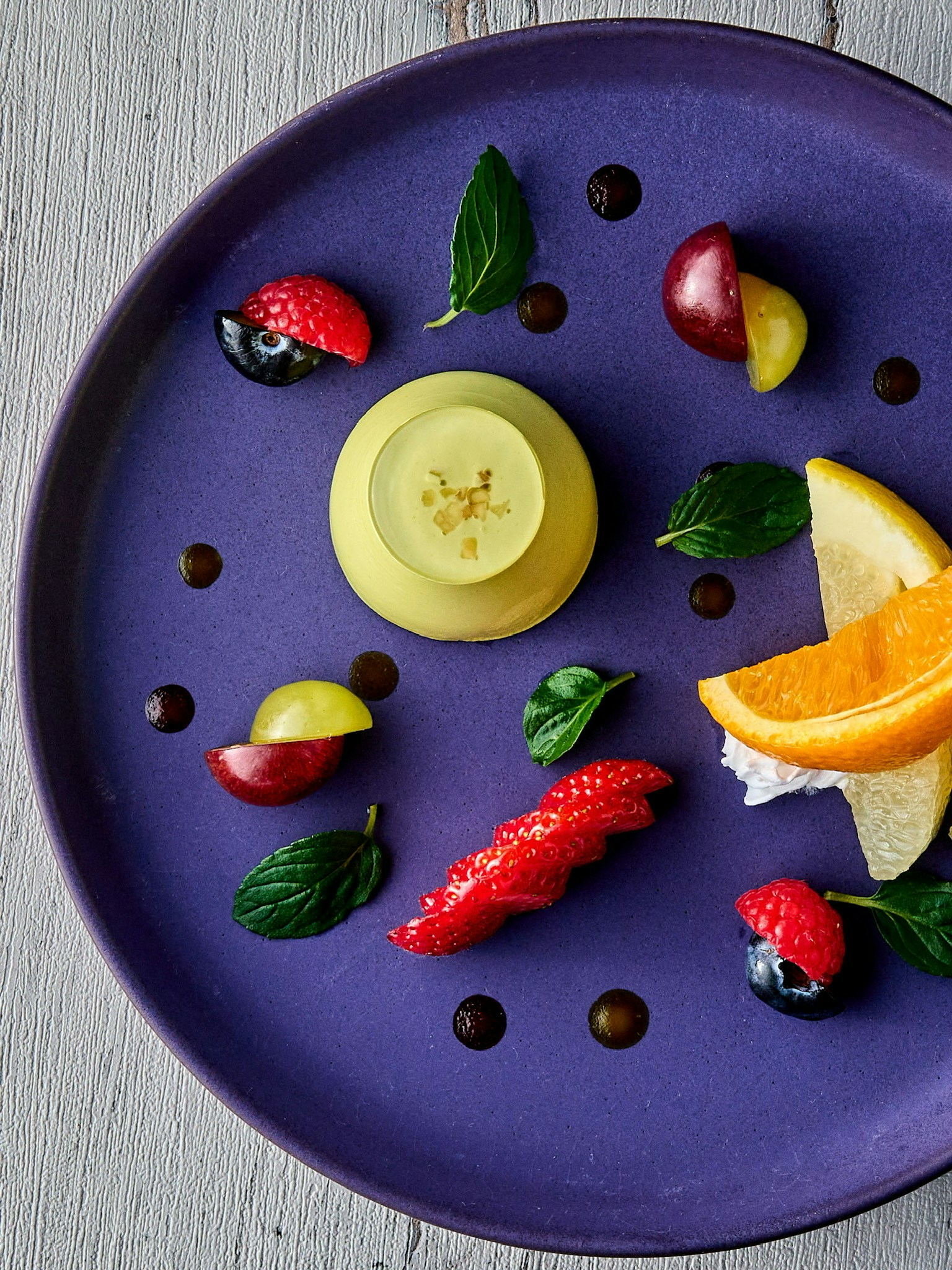 Dessert arranged on a purple plate with fruits and mint leaves
