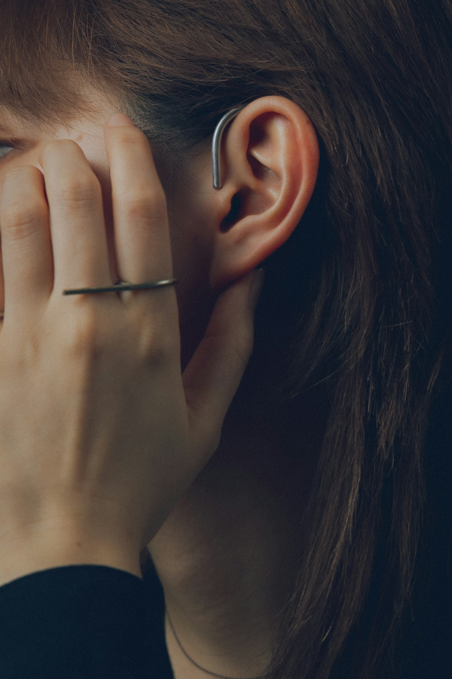 Image d'une main touchant le visage avec un écouteur visible dans l'oreille