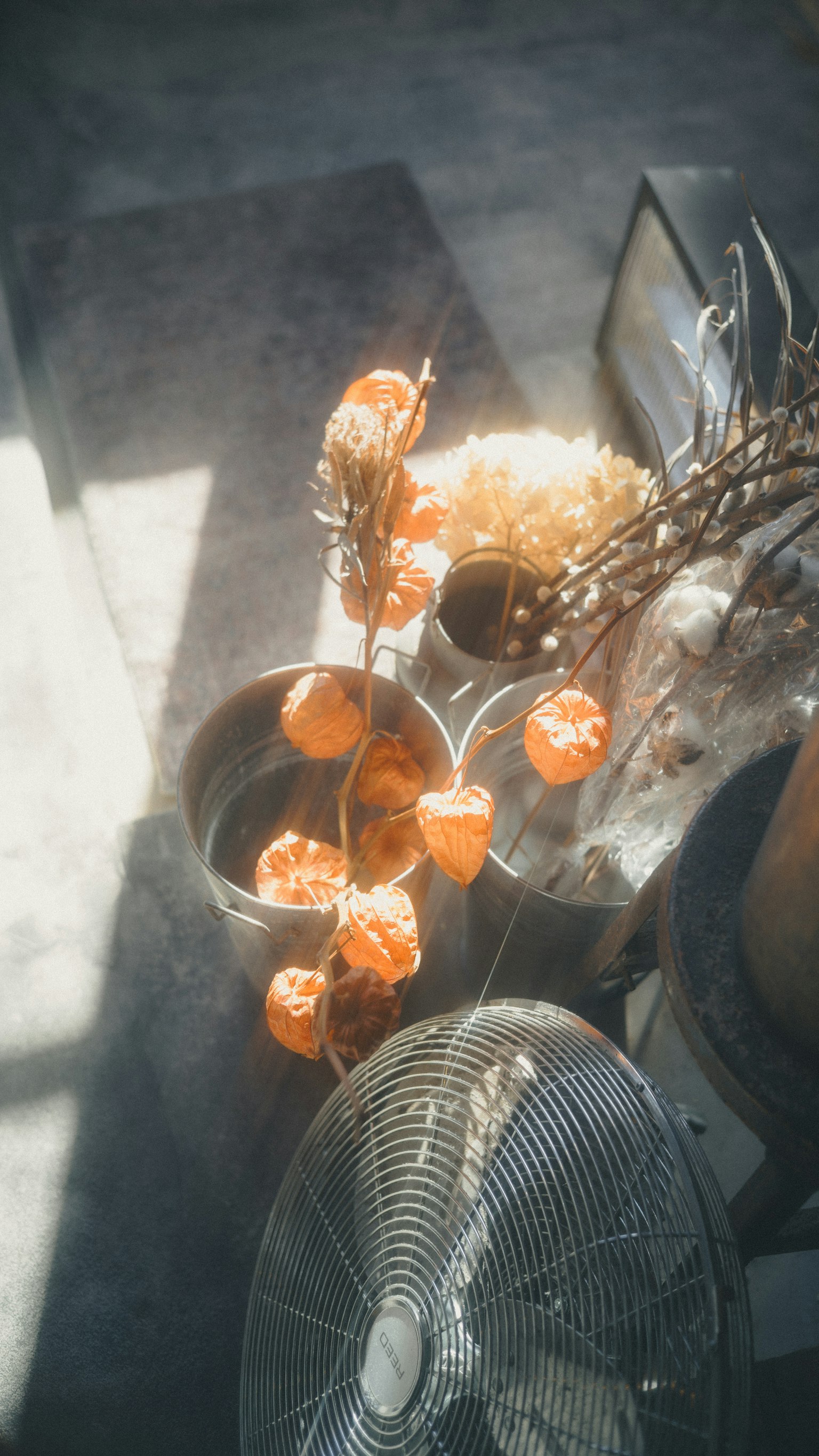 オレンジ色の花が入った花瓶とファンがある室内の静かな風景