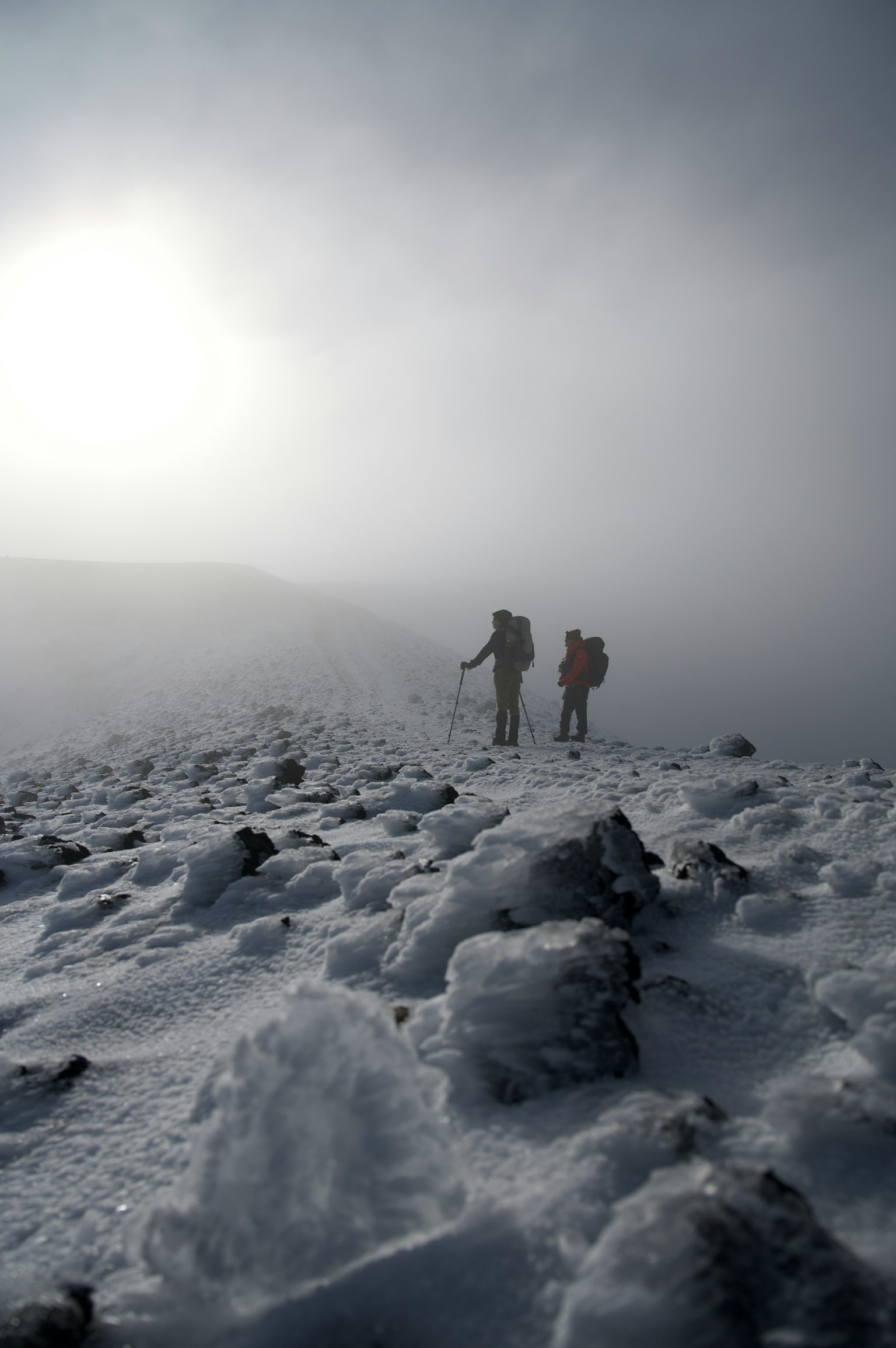 Two hikers walking on a snow-covered mountain path in a foggy landscape