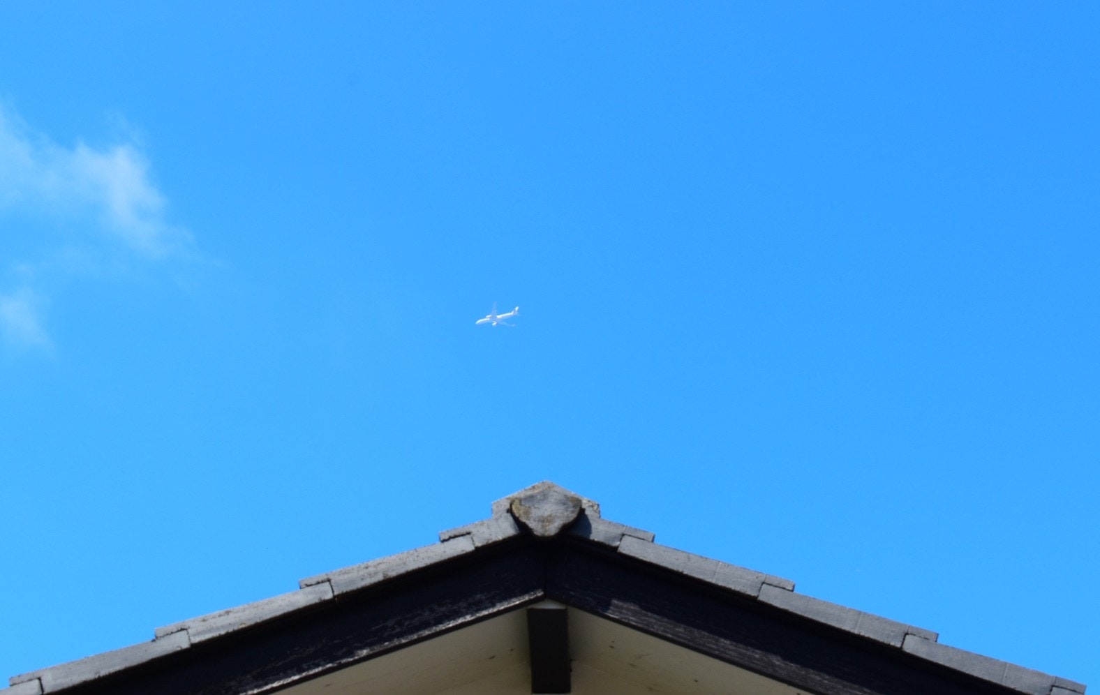 青空の下、屋根の上を飛ぶ飛行機