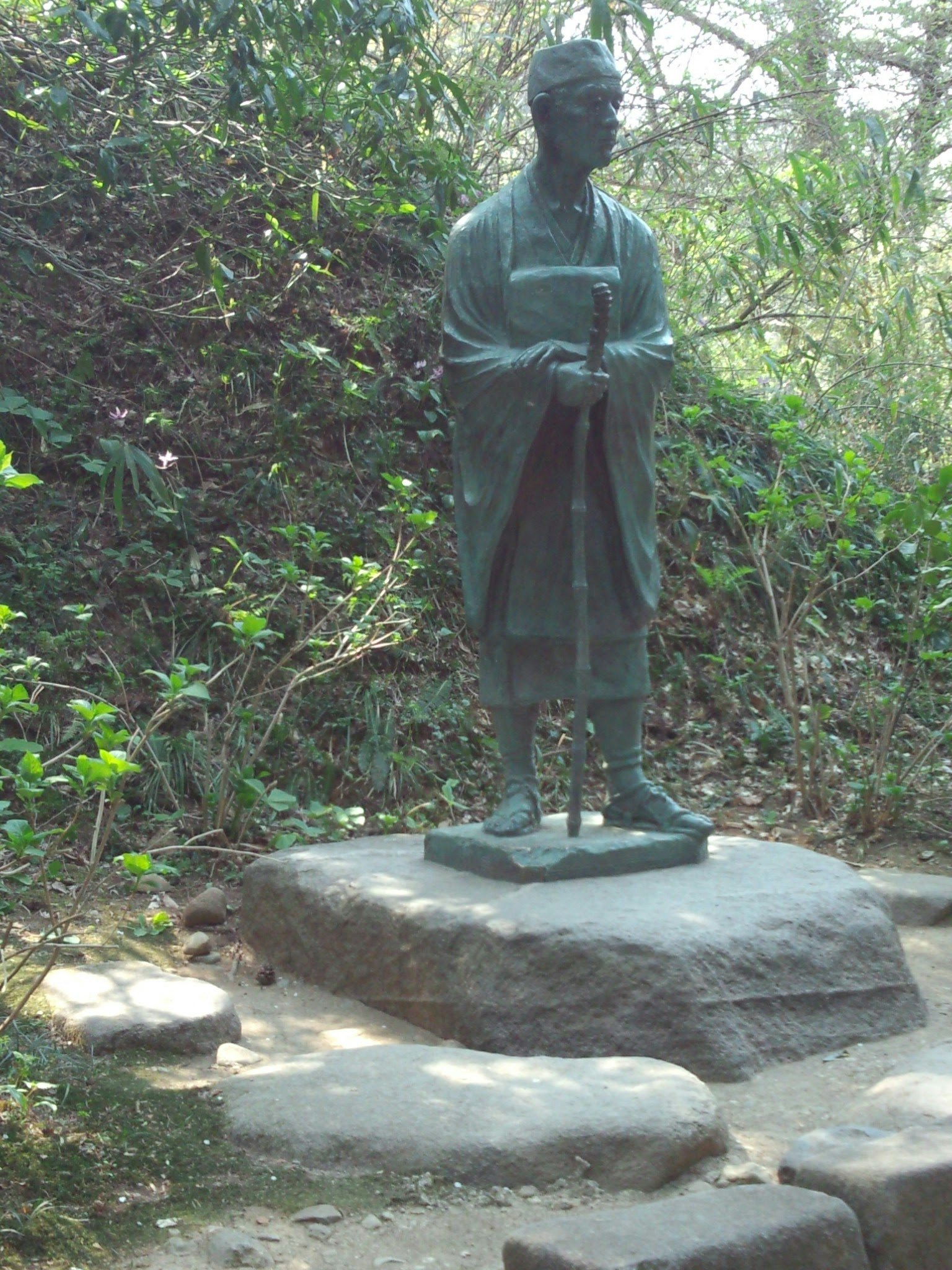 Bronzestatue eines Mannes in einer üppigen grünen Umgebung