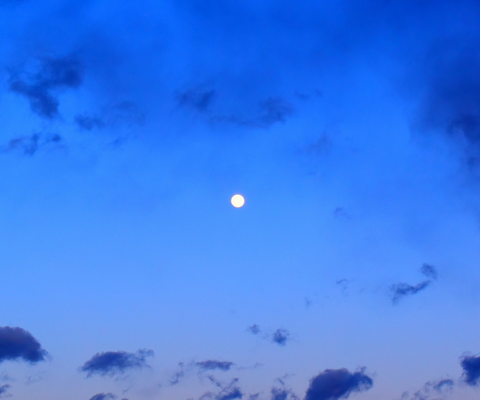 Luna brillante en un cielo azul con nubes dispersas