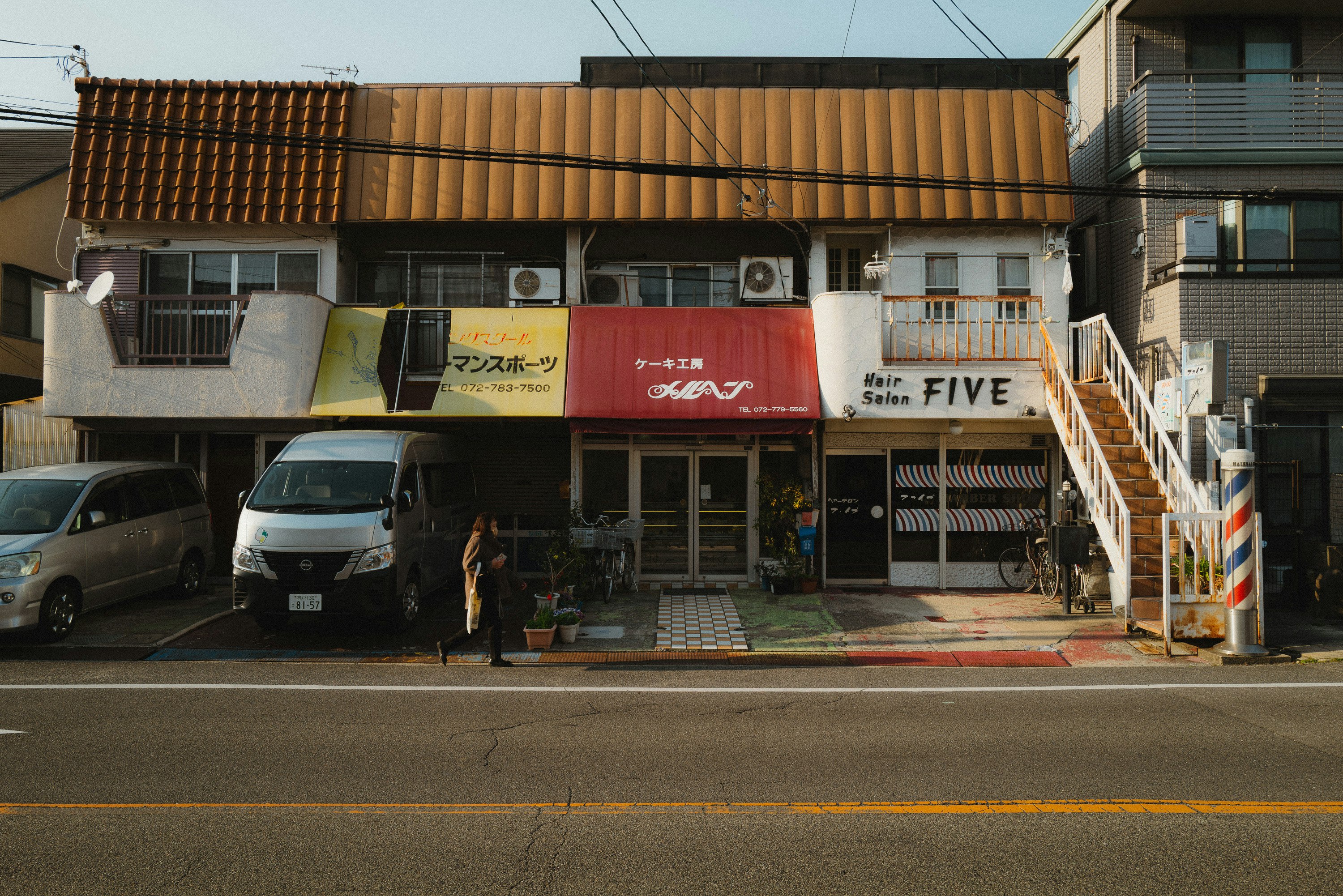 二階建ての店舗の外観、赤いテントと白い看板、周囲に車と人がいる