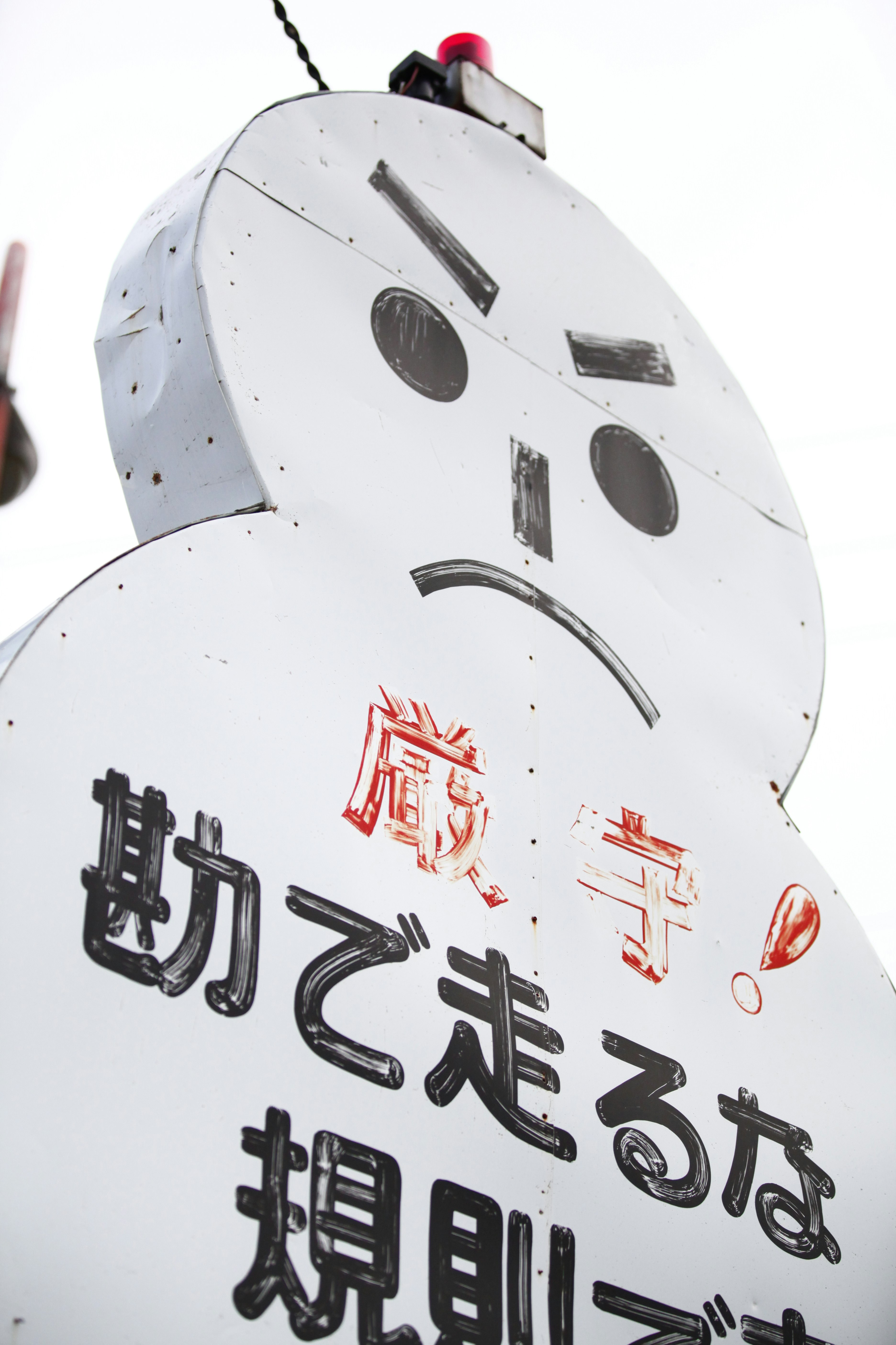 Cartel con forma de robot blanco con texto pintado y rostro