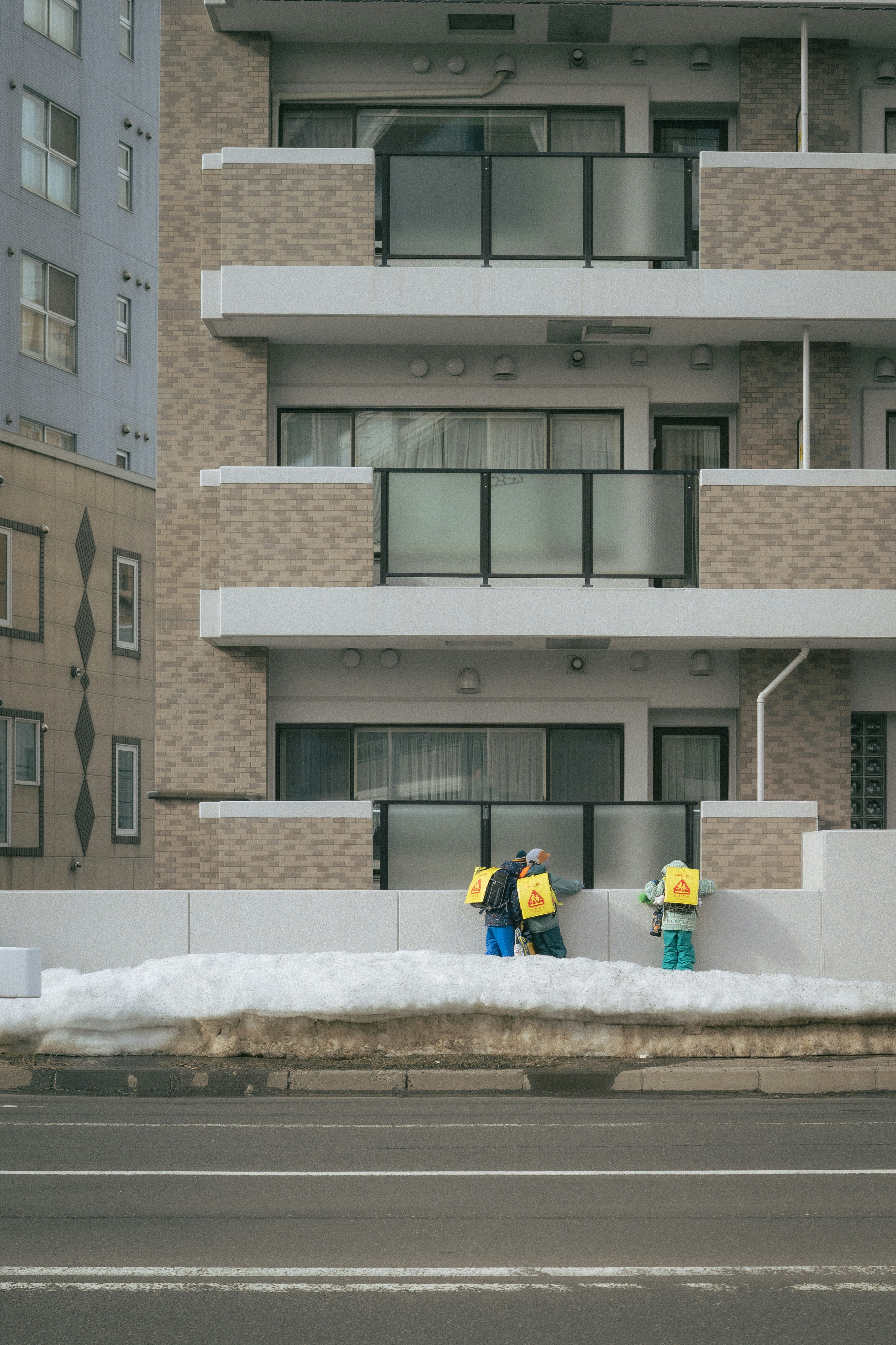 雪の中で作業する二人の作業員とアパートの外観