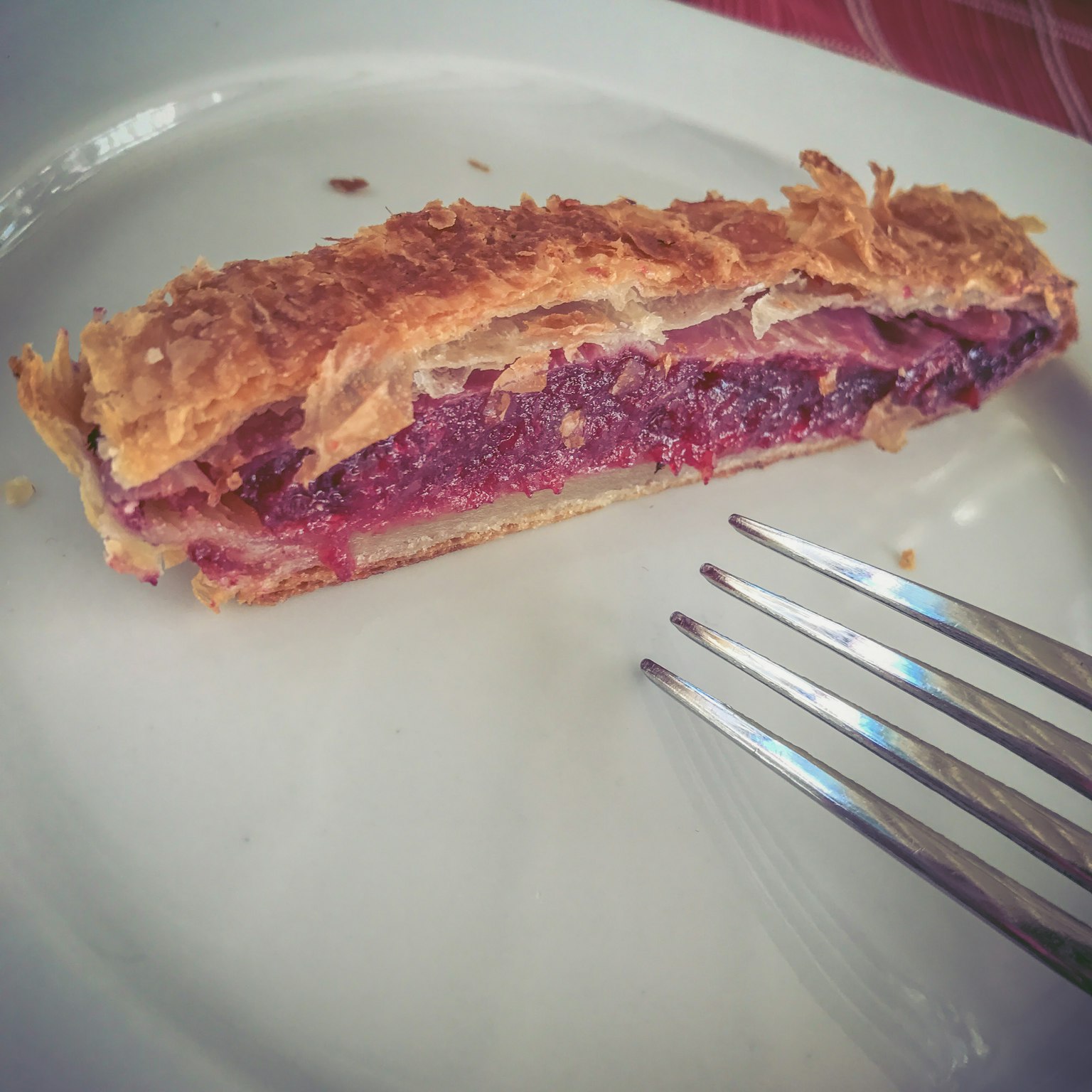 Una fetta di crostata di frutti di bosco su un piatto bianco con una forchetta accanto
