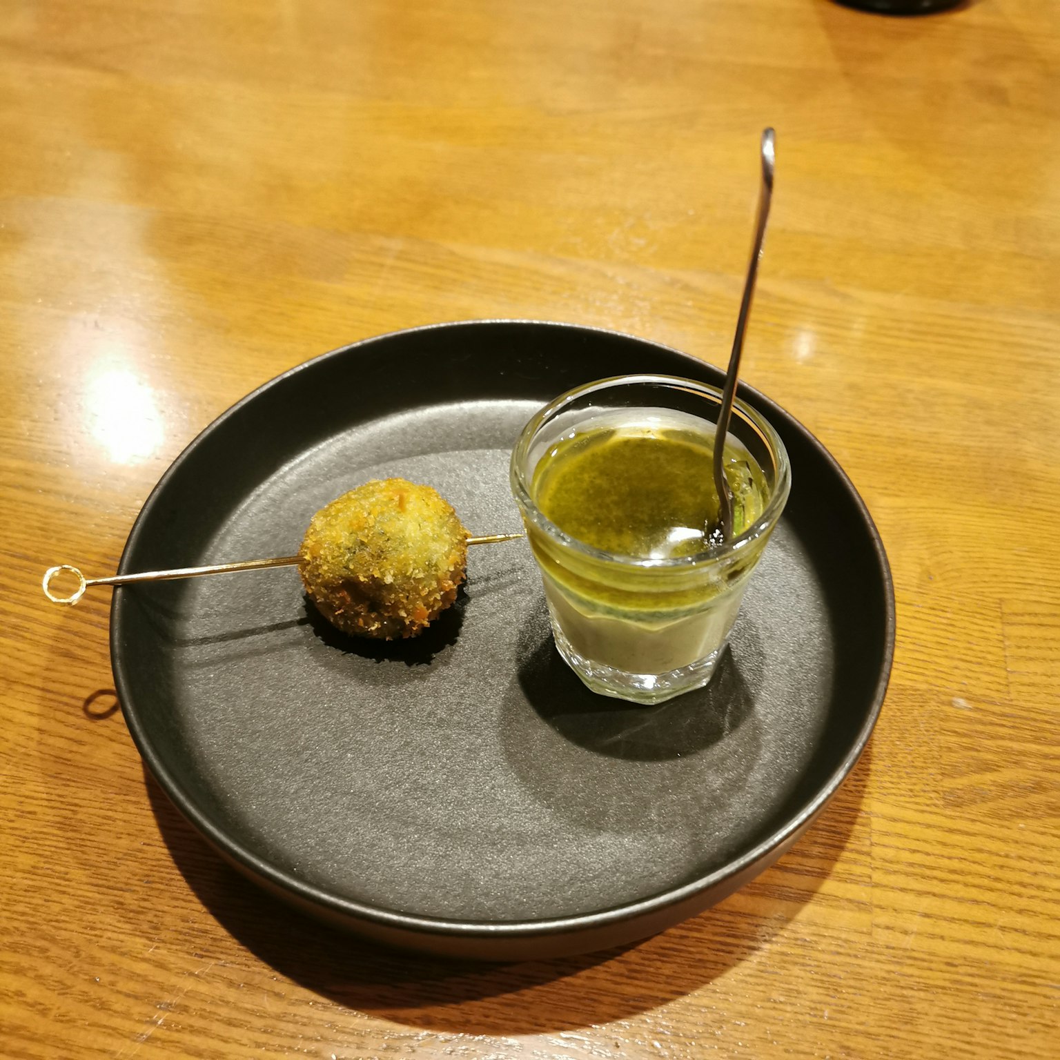 Una pallina fritta su un piatto nero con un piccolo bicchiere di salsa verde