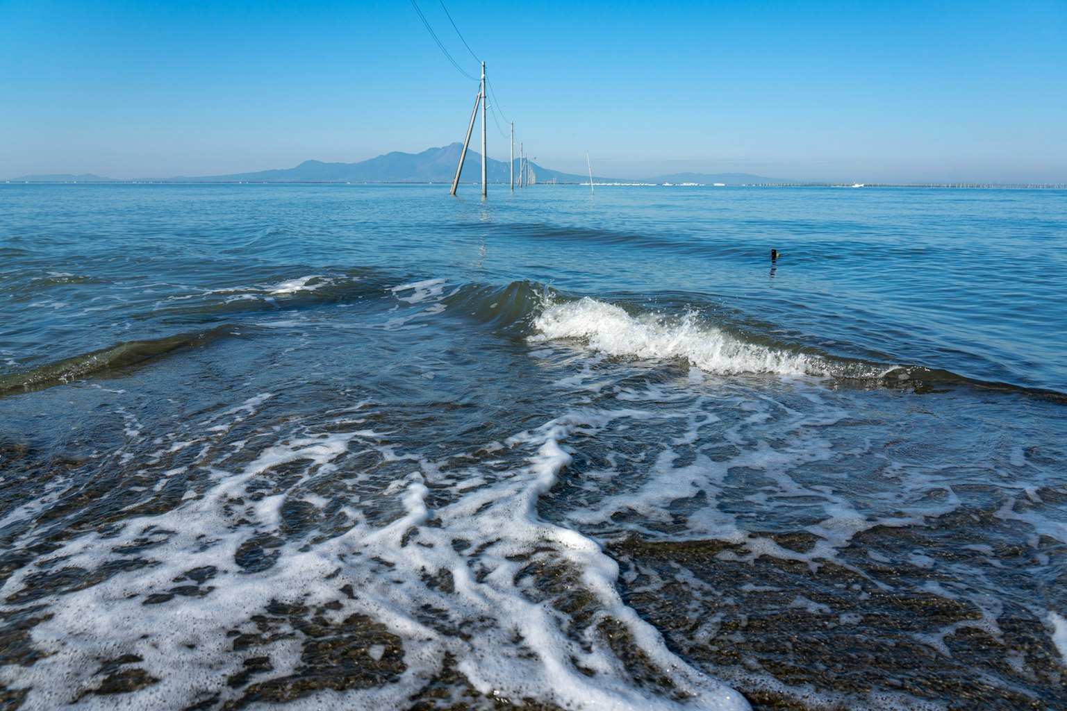 Laut tenang dengan ombak yang menghantam pantai gunung jauh di latar belakang