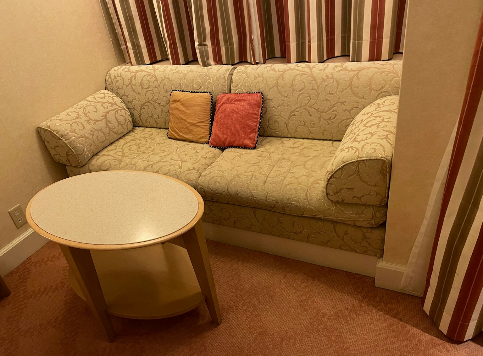 Pequeña sala de estar con un sofá beige y cojines coloridos sobre una mesa redonda