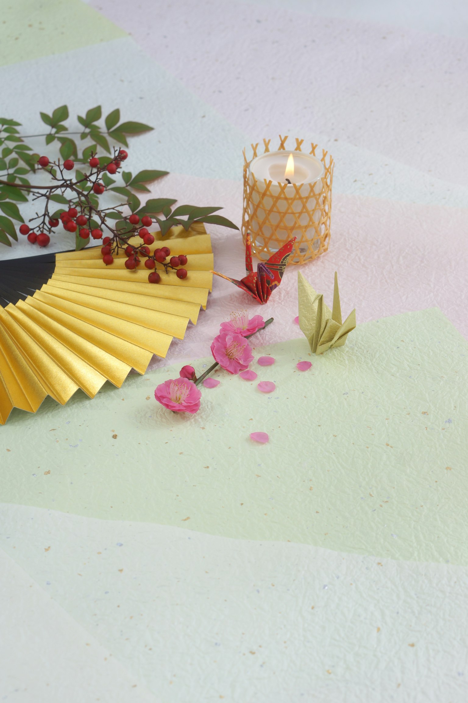 A gold fan with a candle pink petals and green leaves arranged in a serene setting