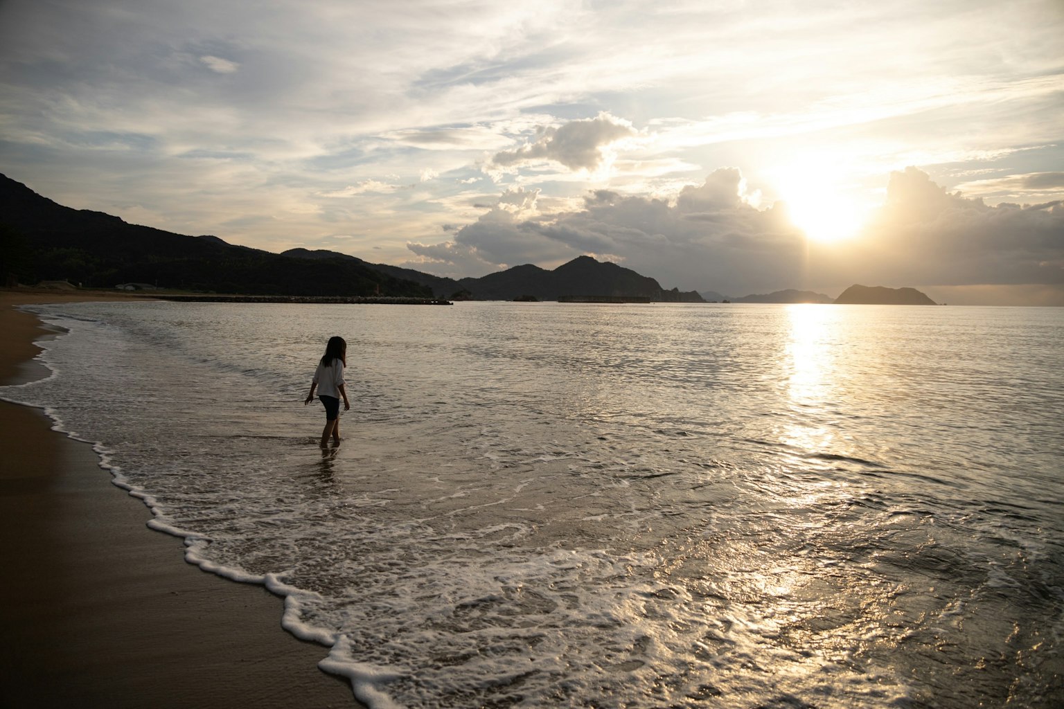 A woman walking along the beach with a beautiful sunset