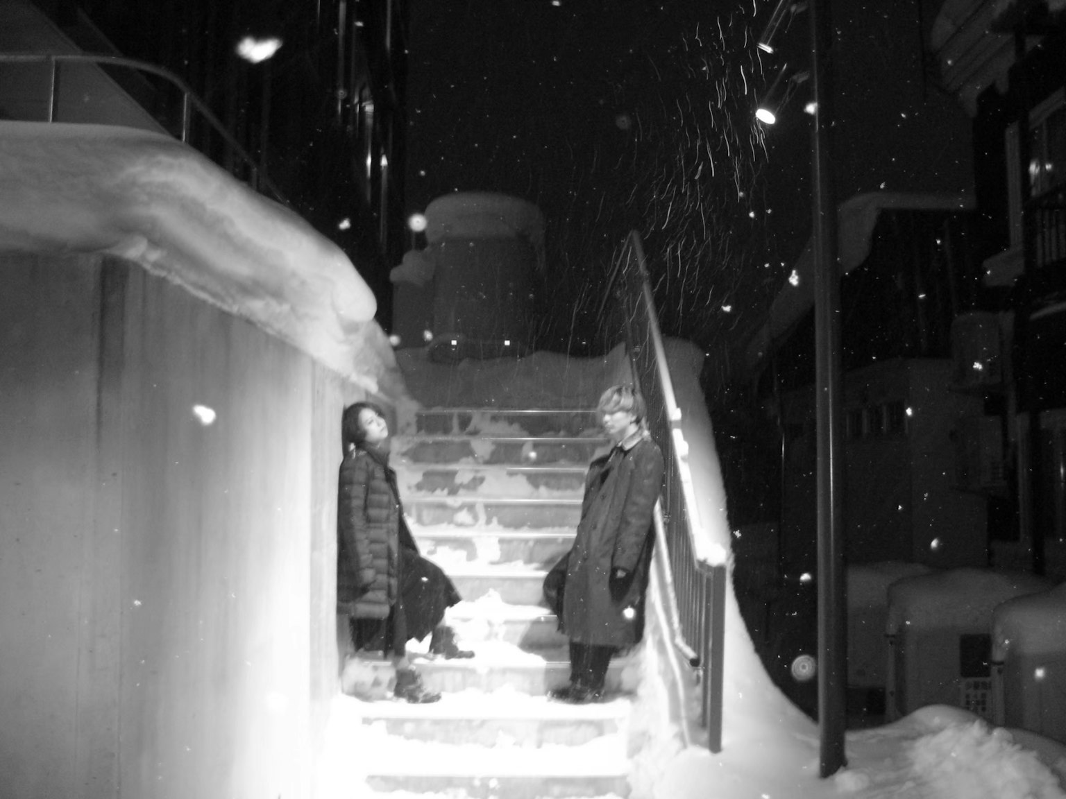 Black and white photo of two people sitting on snowy stairs