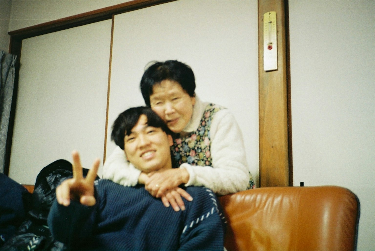 A young man and an elderly woman smiling and posing together in a cozy home setting