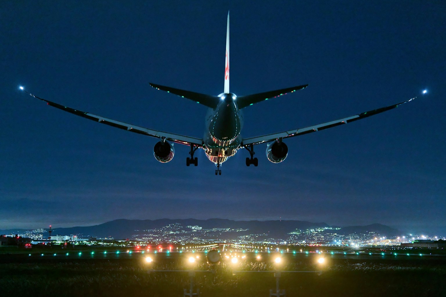 Un avion atterrissant sur une piste la nuit avec des lumières de la ville en arrière-plan