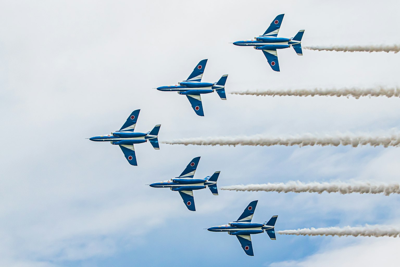 Avions bleus volant en formation avec des traînées de fumée blanche