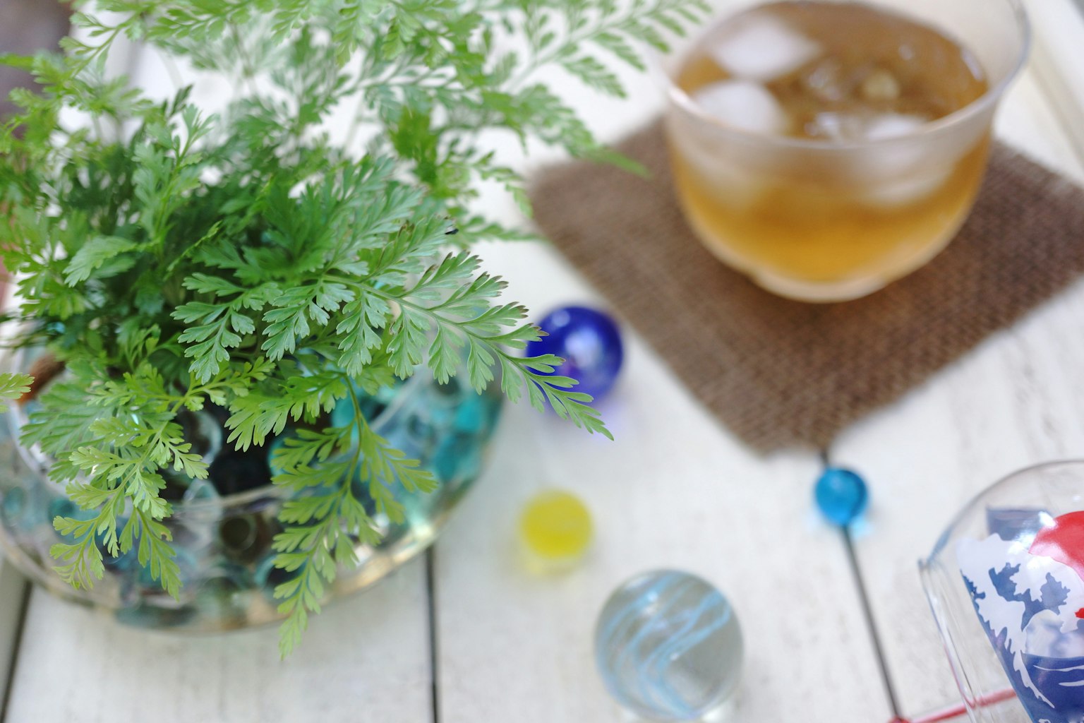Sebuah pemandangan meja yang tenang dengan tanaman hijau dan gelas minuman dalam mangkuk transparan