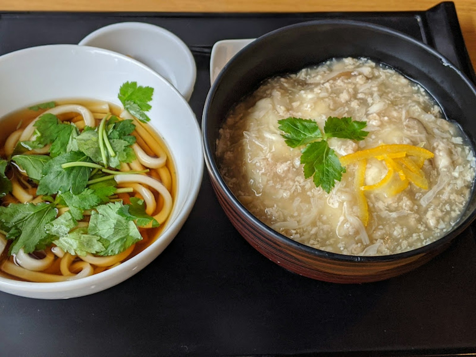 Semangkuk mie udon dengan ketumbar dan semangkuk bubur dihiasi ketumbar dan lemon