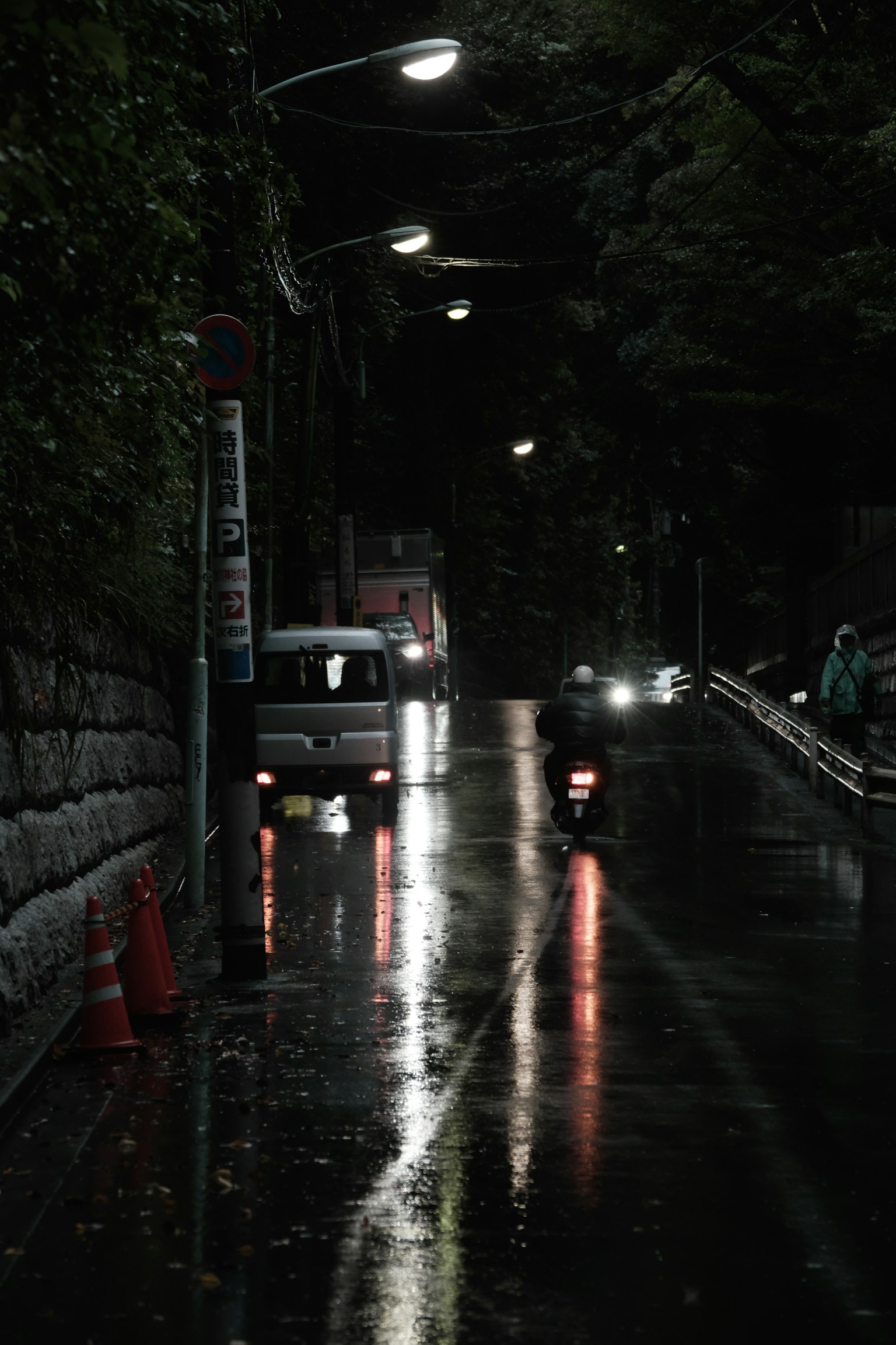 Jalan gelap di malam hari dengan refleksi lampu jalan dan hujan