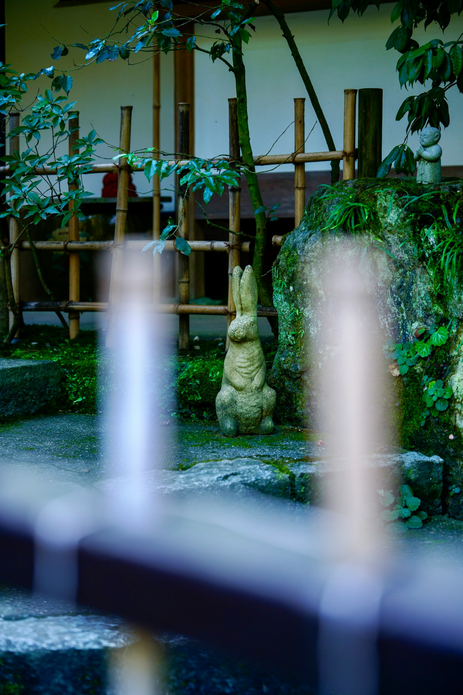 Pemandangan taman Jepang dengan patung kelinci dan struktur bambu