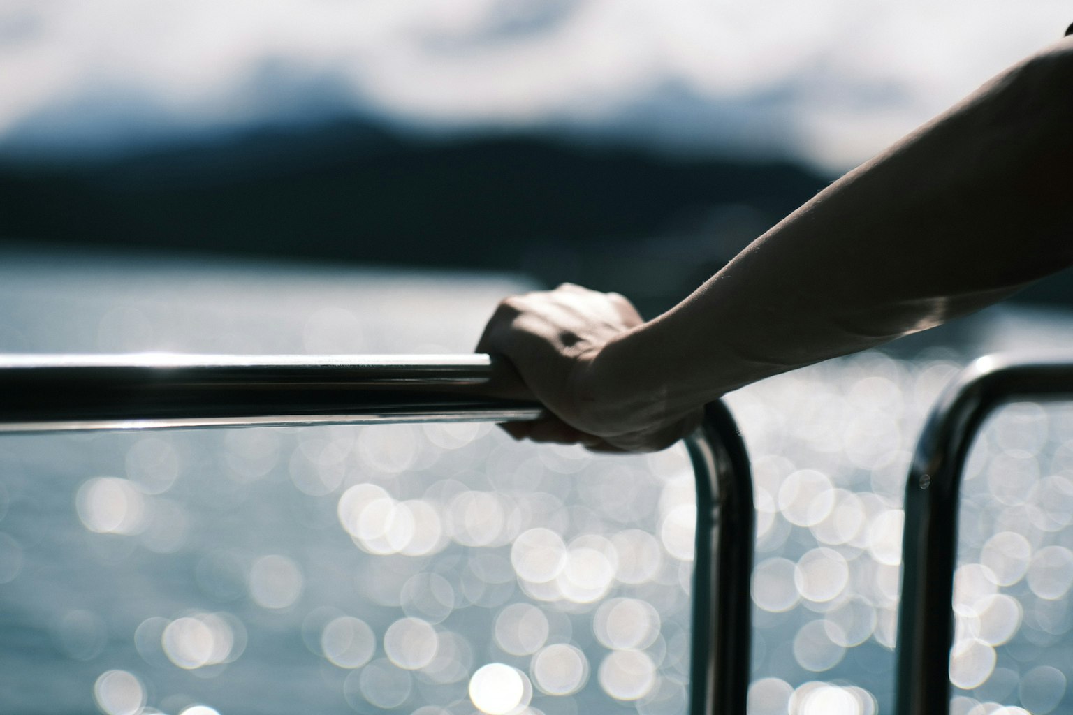Close-up of a hand gripping a metal railing overlooking a shimmering water surface