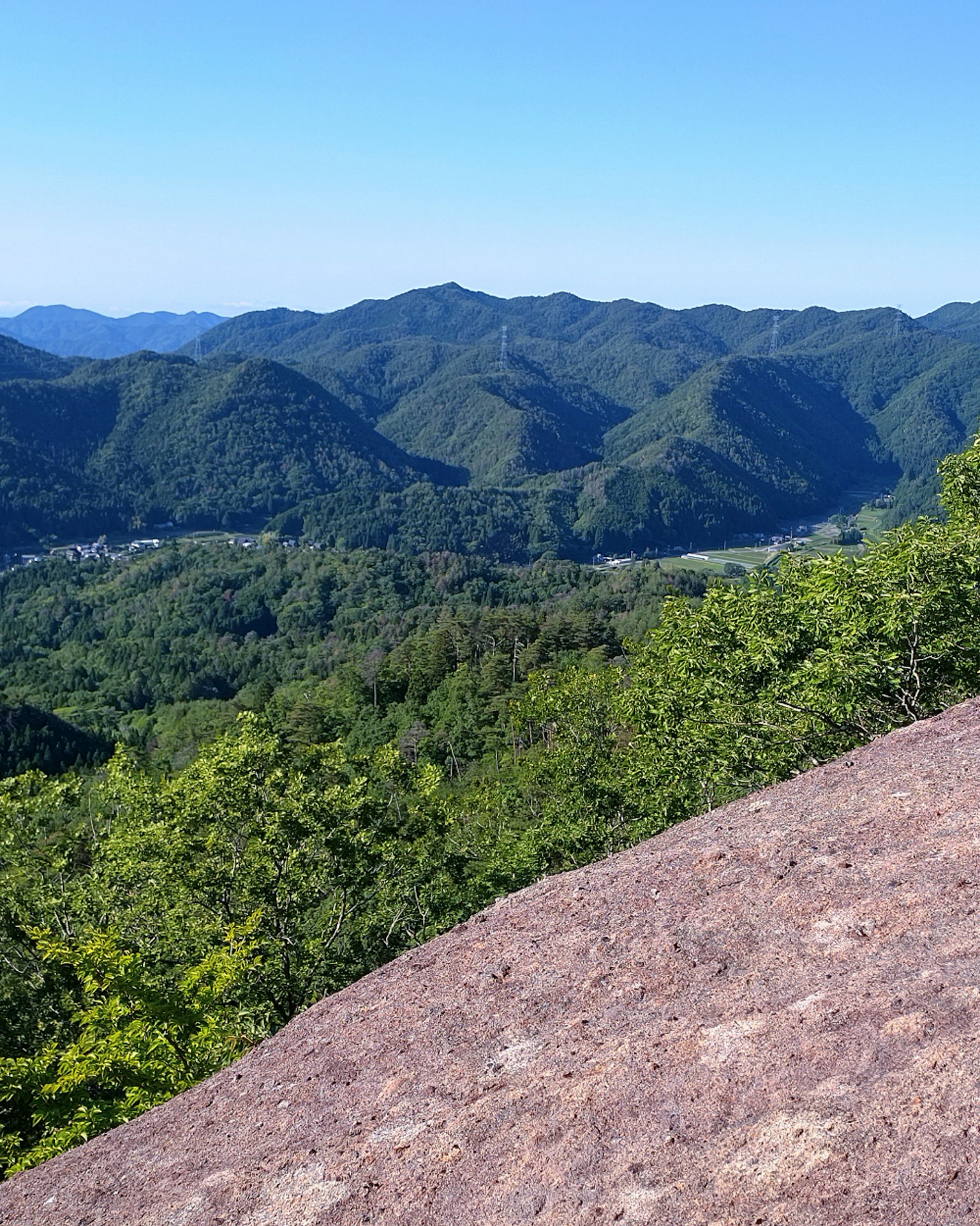 Vista de montañas verdes y valles desde una roca bajo un cielo azul claro