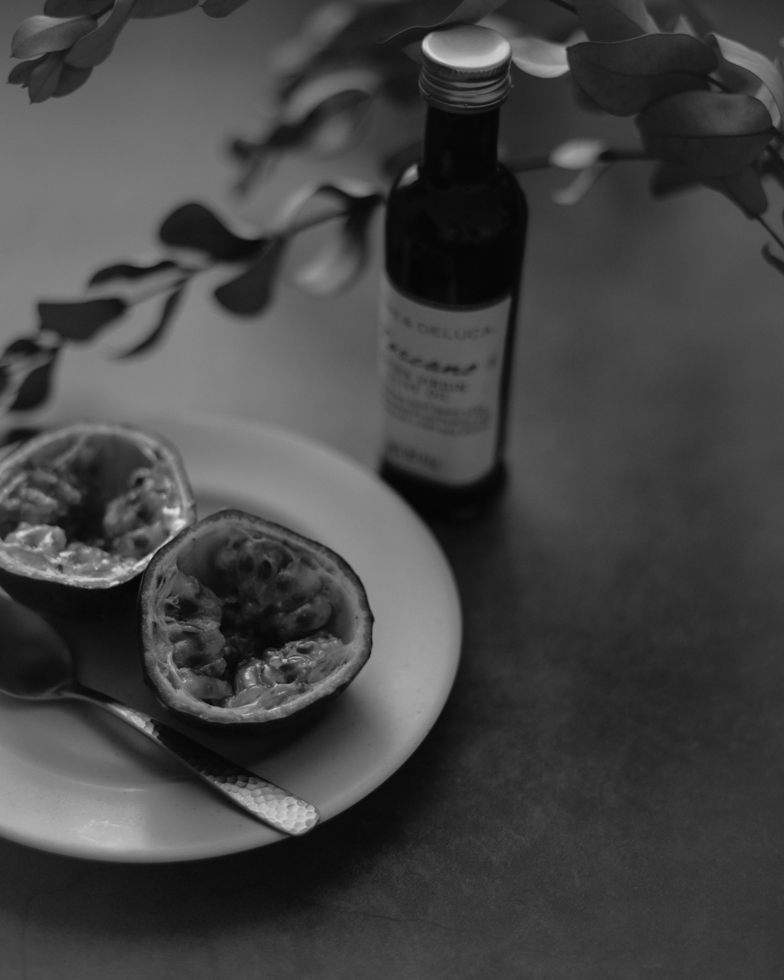 Une assiette avec des moitiés de fruit de la passion et une cuillère à côté d'une bouteille en noir et blanc