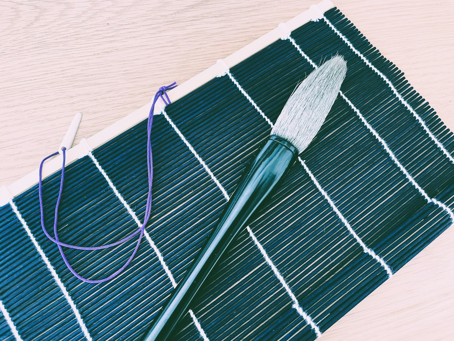 Großer Pinsel und lila Schnur auf einer schwarzen Bambusmatte