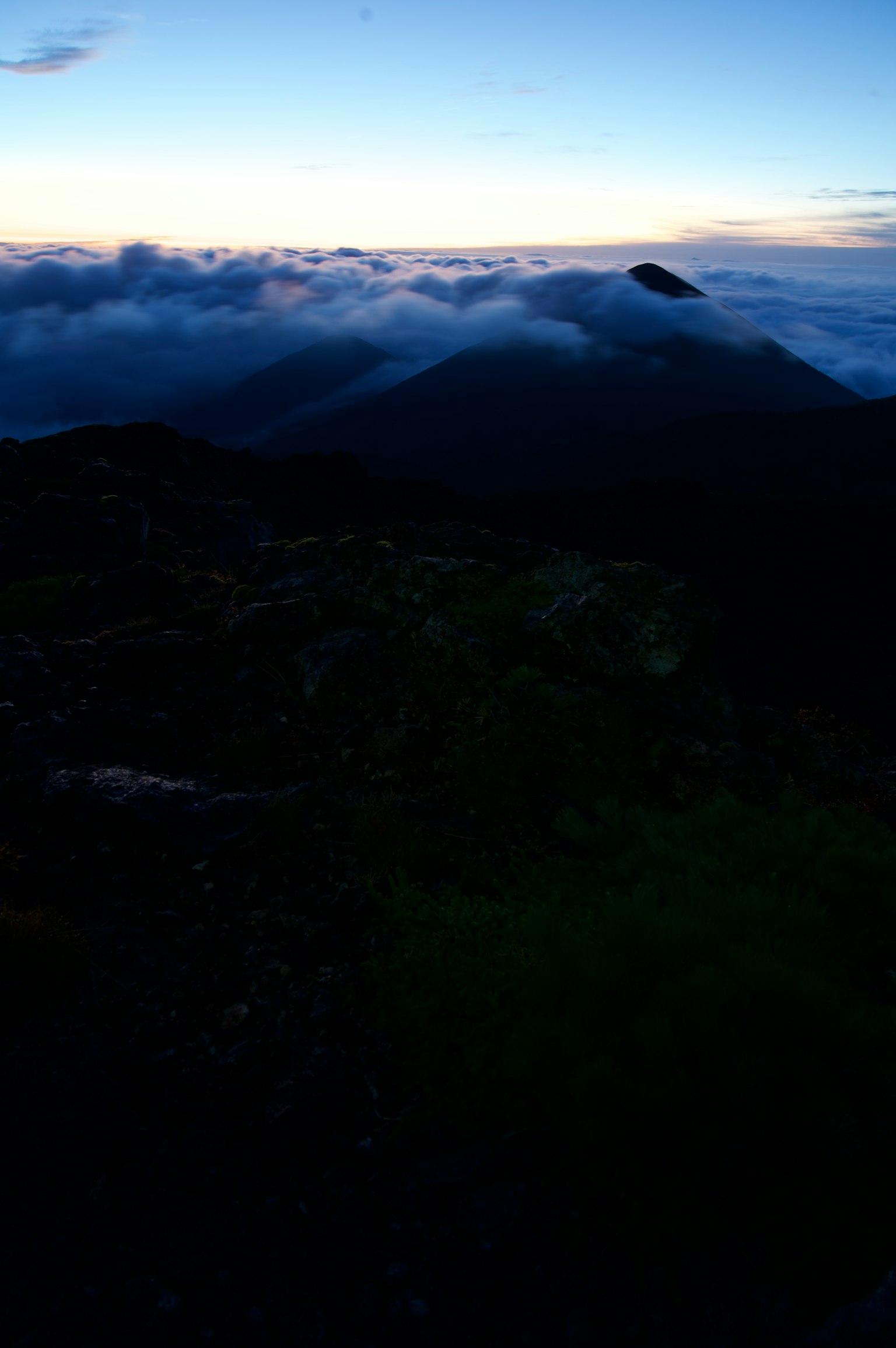 Twilight landscape from mountain peak with clouds below and distant mountains