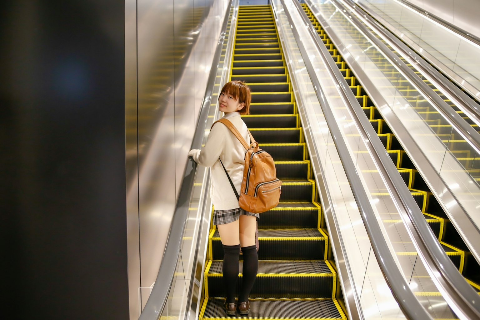 Femme debout sur un escalateur avec des lignes jaunes et une tenue élégante