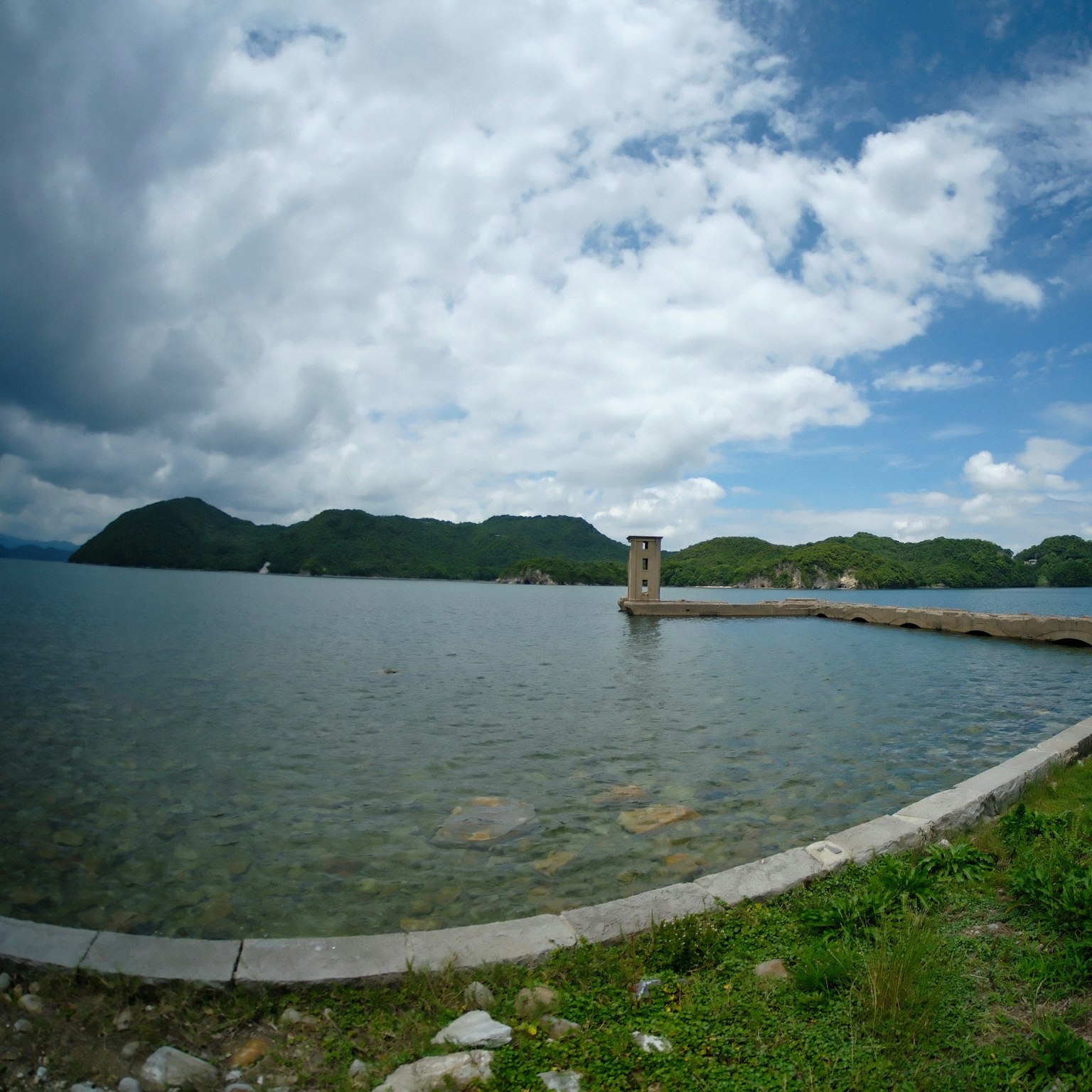 Vista panoramica di una torre di pietra vicino al lago con montagne verdi sullo sfondo